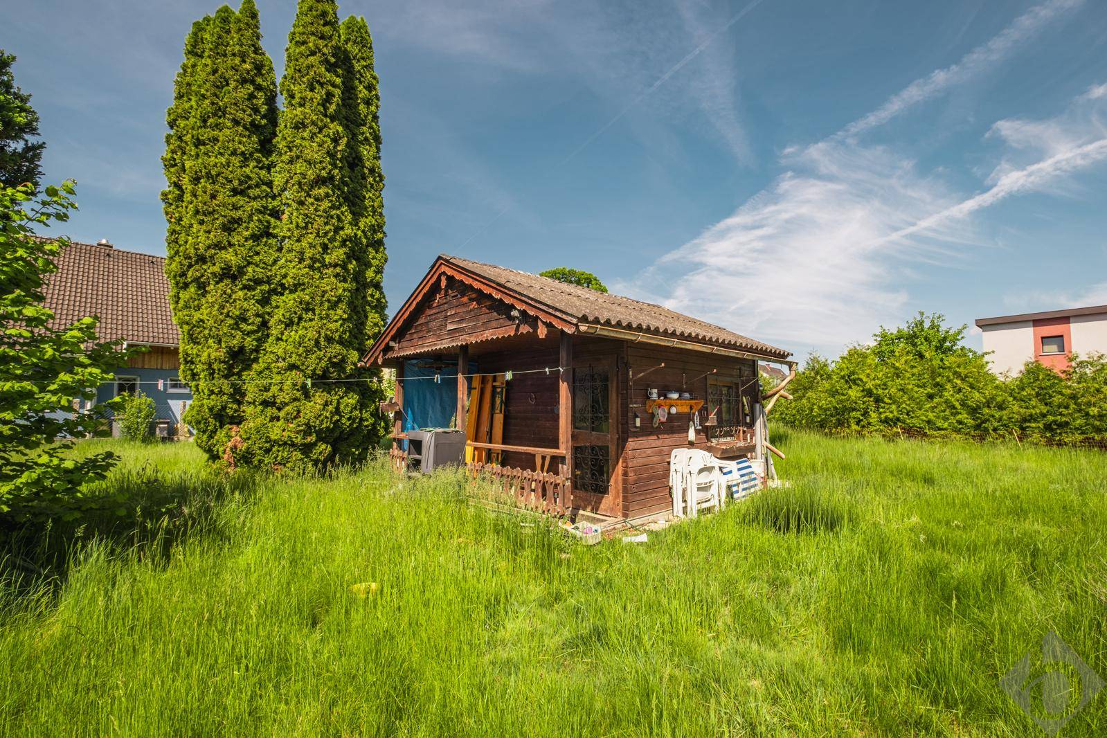 Rustikales Holzgartenhaus mit kleiner Veranda auf einem sonnigen Wiesengrundstück.