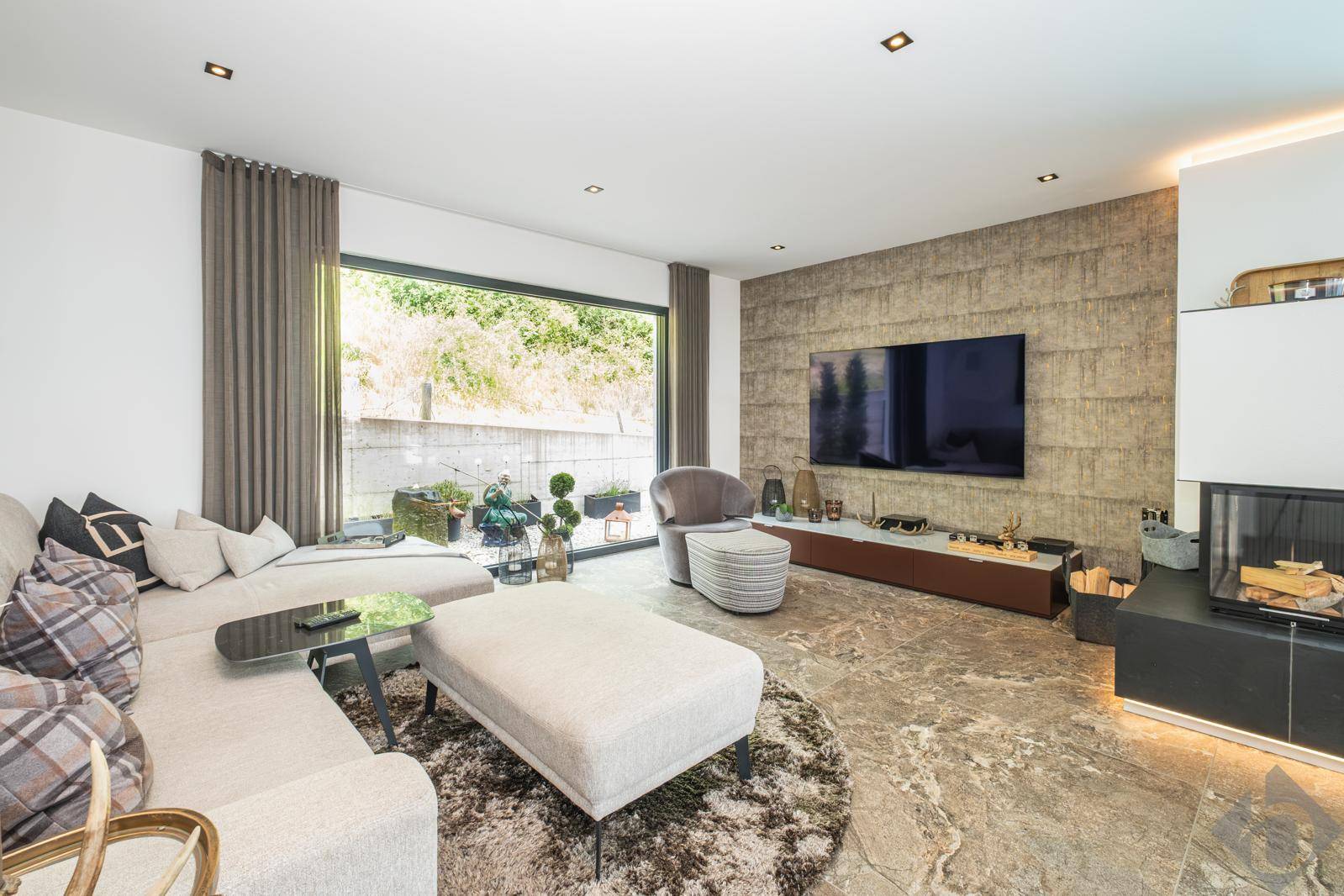 Gemütliches Wohnzimmer mit großem Sofa, modernem Kamin und Zugang zu einem kleinen Außenbereich.