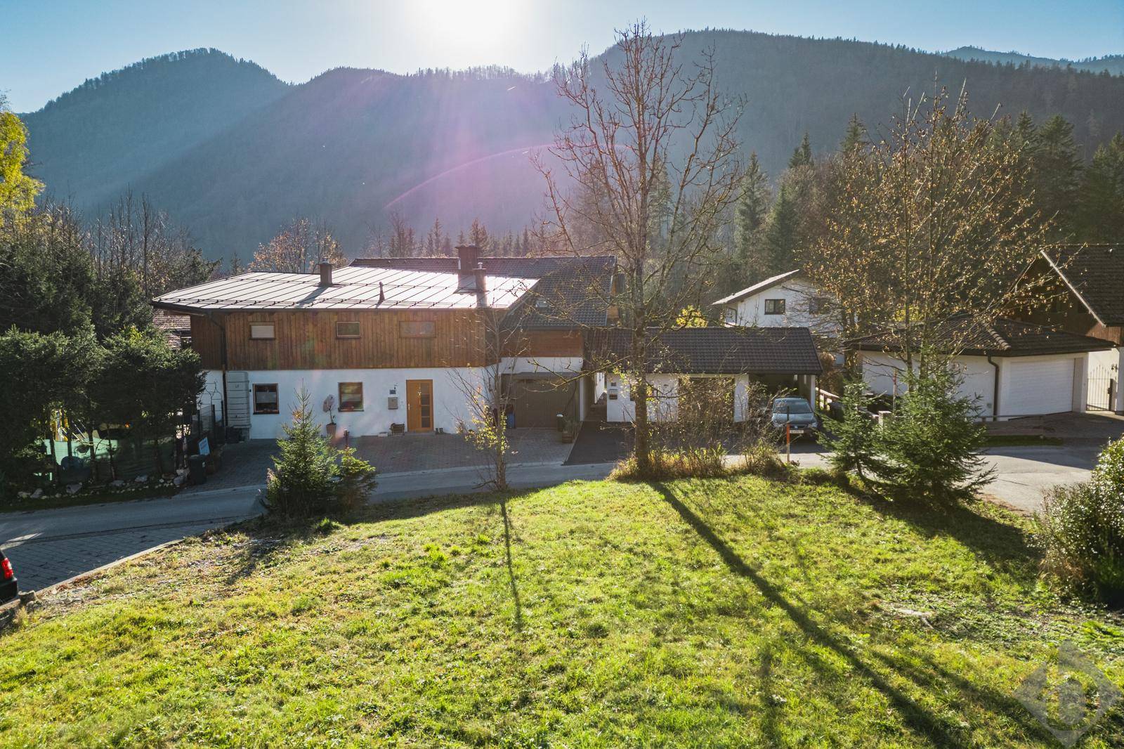Haus mit Holzfassade und weißem Putz, umgeben von einem grünen Garten und majestätischen Bergen im Hintergrund.