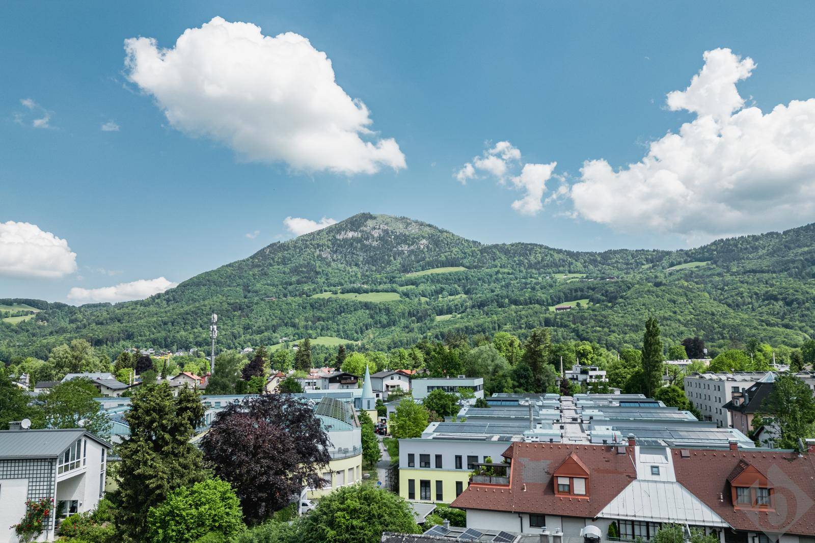 Blick über eine Stadt mit vielfältiger Bebauung und bewaldeten Hügeln im Hintergrund.