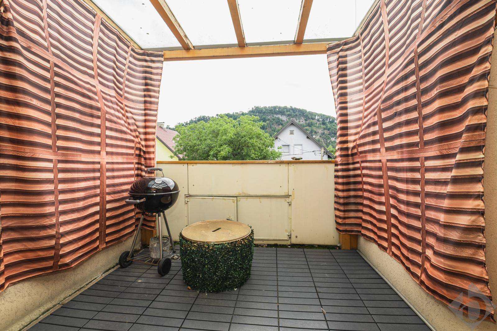 Überdachter Balkon mit Grill, Sitzgelegenheit und Blick auf die umliegende Hügellandschaft.