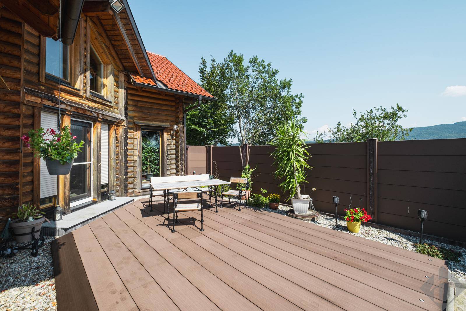 Geräumige Holzterrasse mit Sitzgelegenheiten vor einem charmanten Holzhaus unter blauem Himmel.