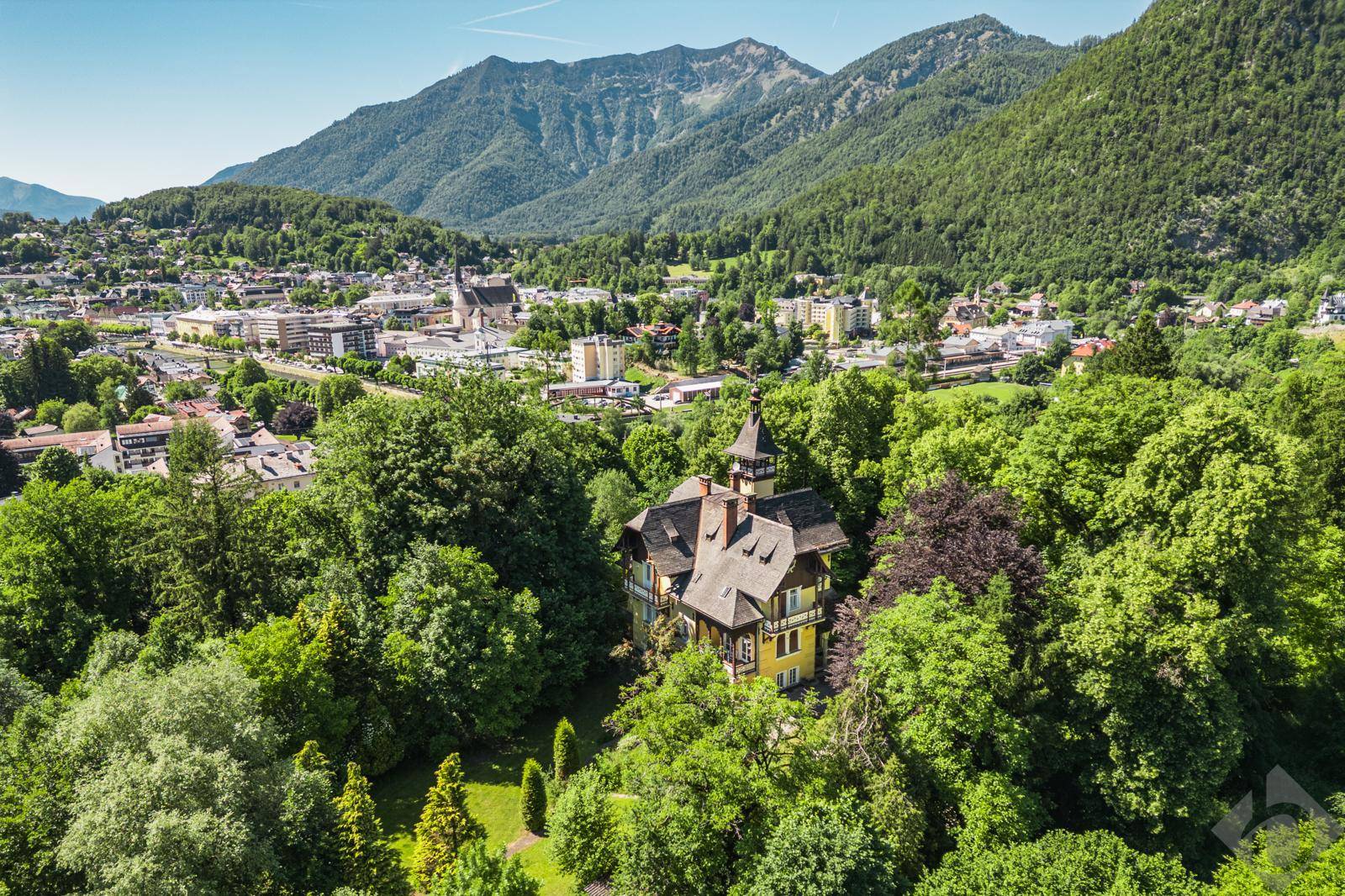 Weitläufige Luftaufnahme der historischen Villa, eingebettet in eine grüne Landschaft mit Stadt und Bergen im Hintergrund.