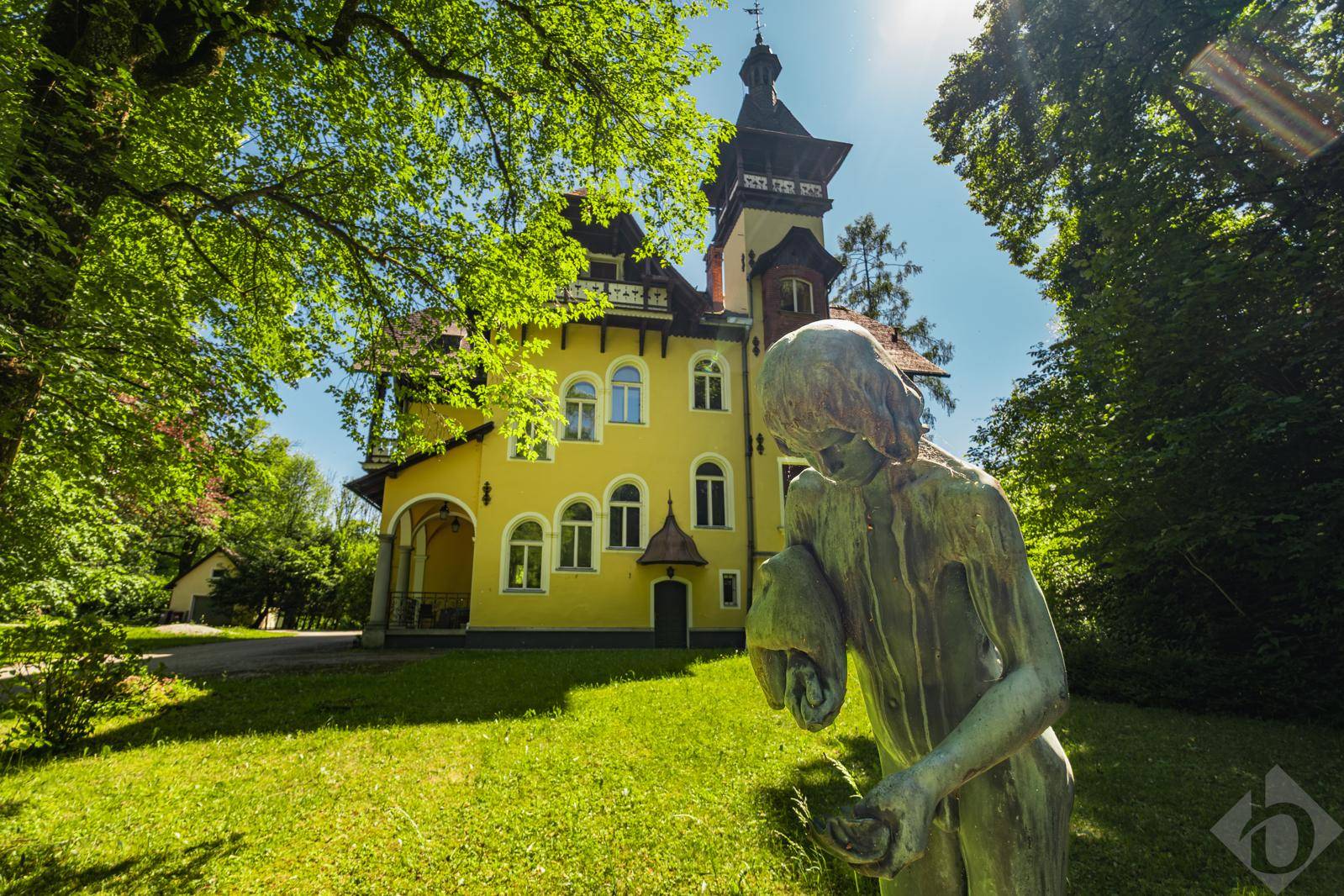 Die historische gelbe Villa mit kunstvoller Fassade und einem Garten mit Skulptur unter strahlendem Sonnenschein.