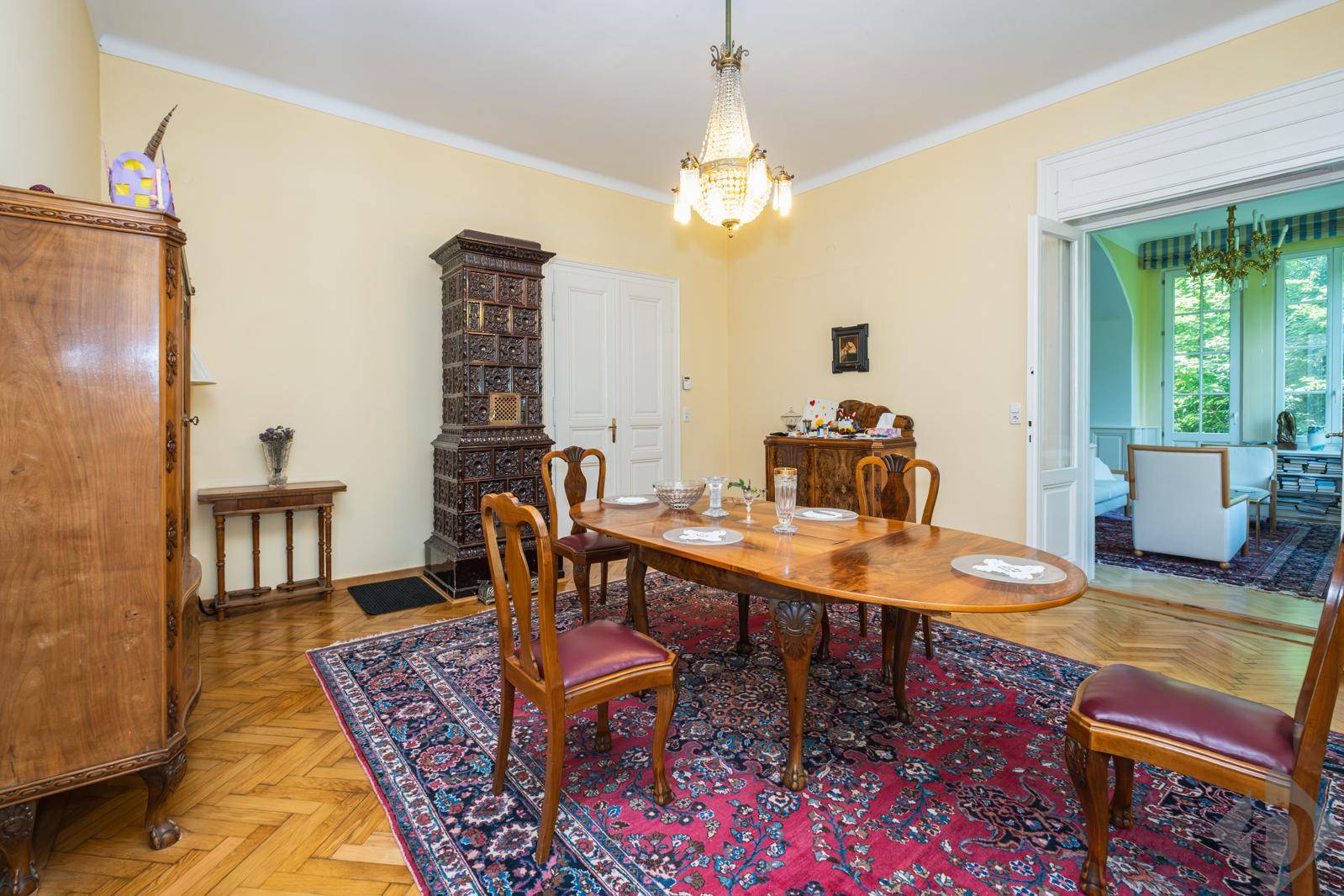 Elegantes Esszimmer mit antikem Holztisch, Kachelofen und Parkettboden, verbunden mit einem weiteren Wohnbereich.