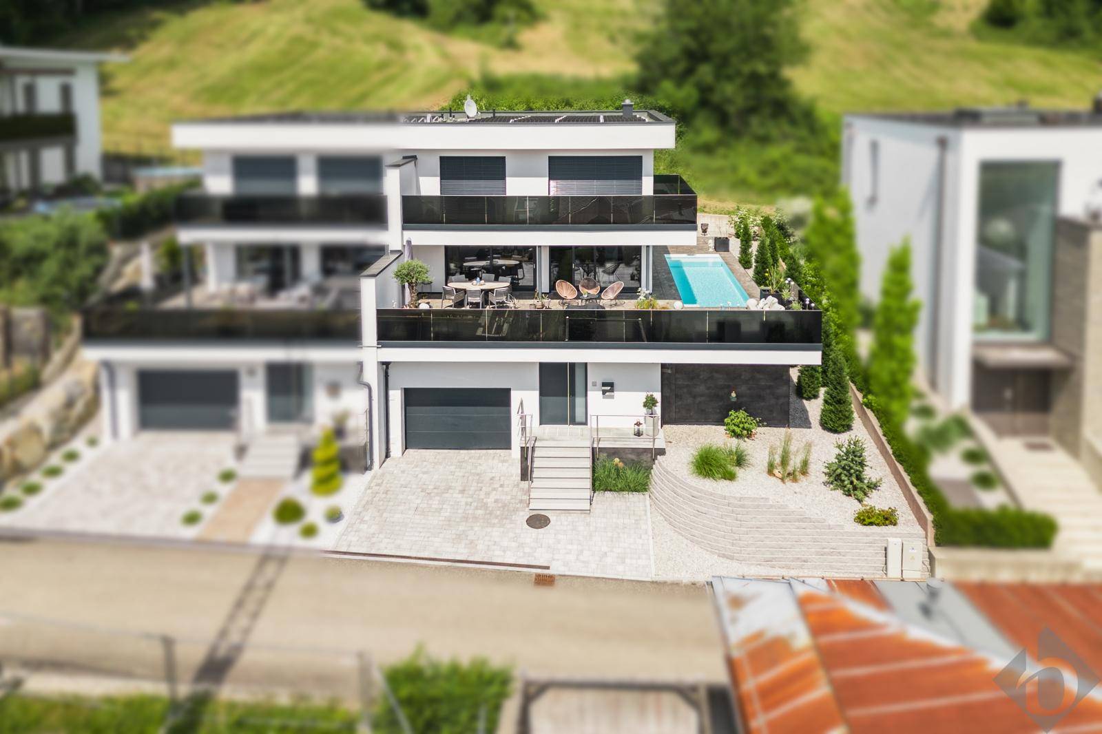 Moderne Villa mit mehreren Terrassen, Pool und ansprechender Architektur in grüner Umgebung.