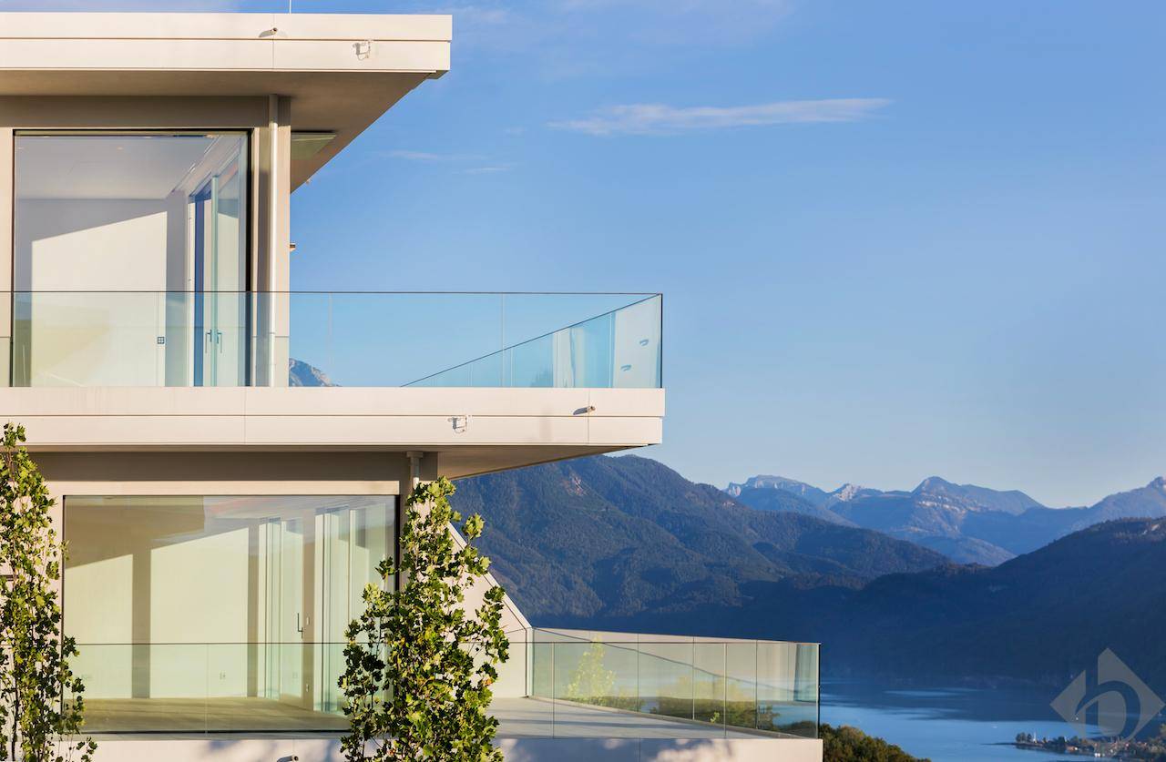 Moderne Architektur mit Glasbalkonen und atemberaubendem Blick auf Berge und See.