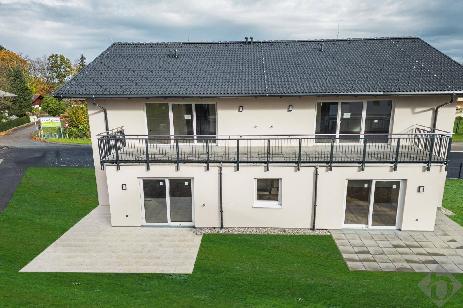 Moderne Hausfassade mit Balkonen, gepflasterten Terrassen und einem gepflegten Rasenbereich.