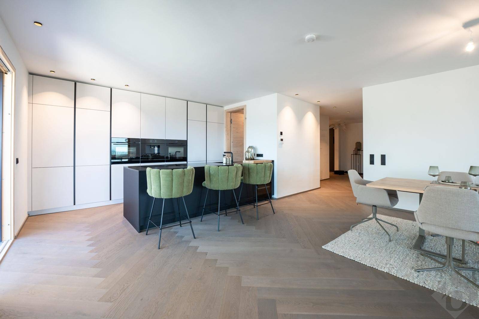 Moderne offene Küche mit Kochinsel und Essbereich, ausgestattet mit hochwertigen Geräten und Parkettboden.