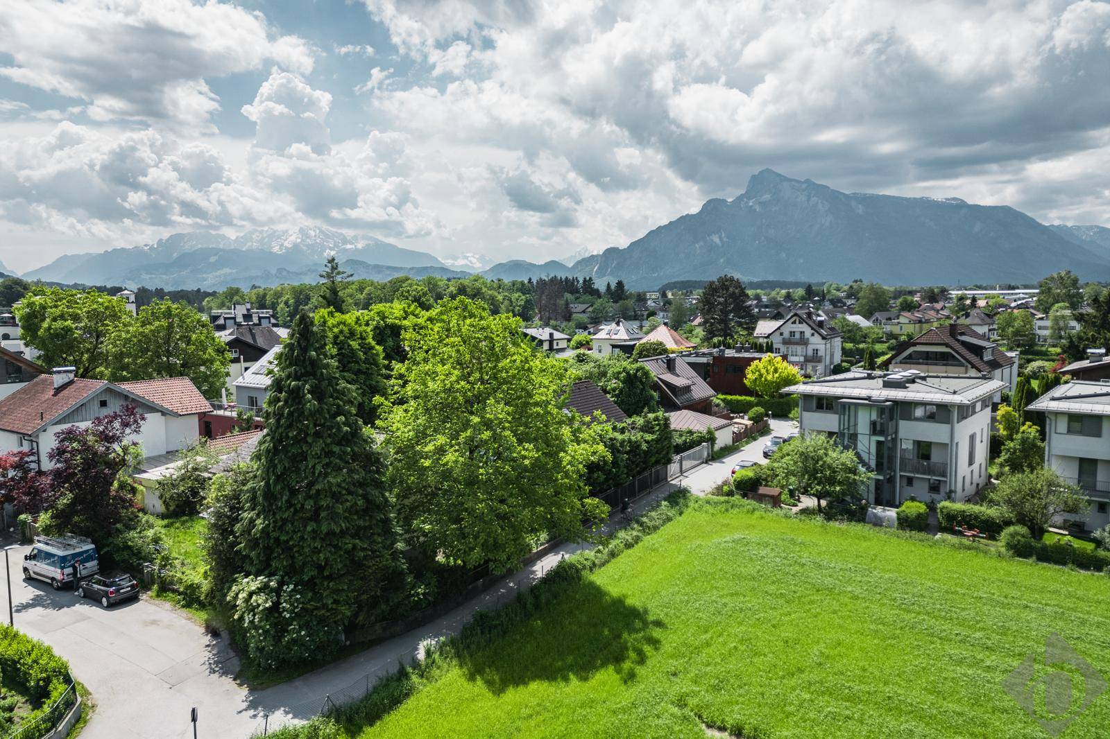 Weitläufiger Blick über eine Wohngegend mit grünen Wiesen und beeindruckender Bergkulisse.