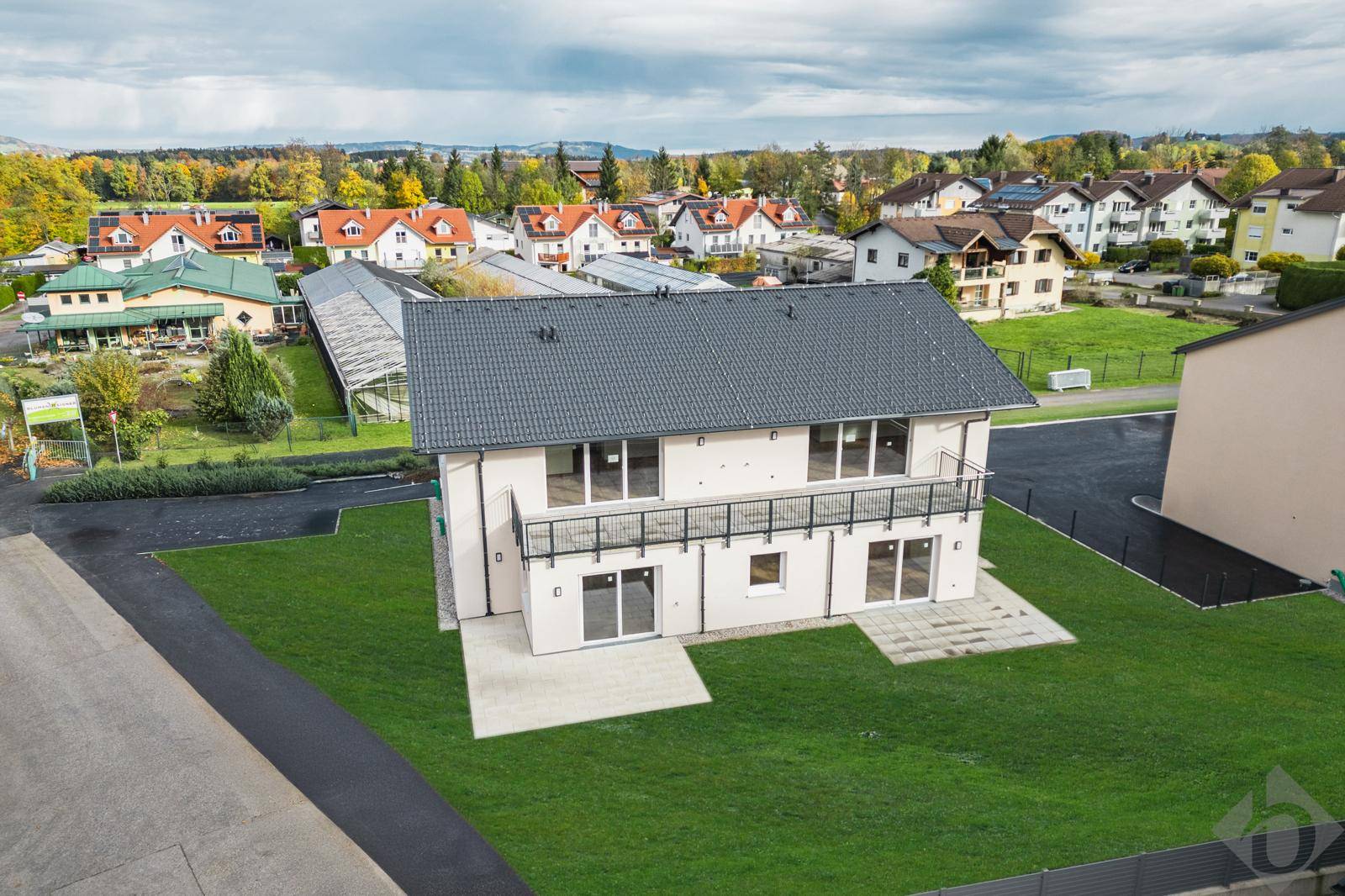 Ansicht des modernen Hauses mit Balkonen, Terrassen und einem weitläufigen Rasenbereich in grüner Umgebung.