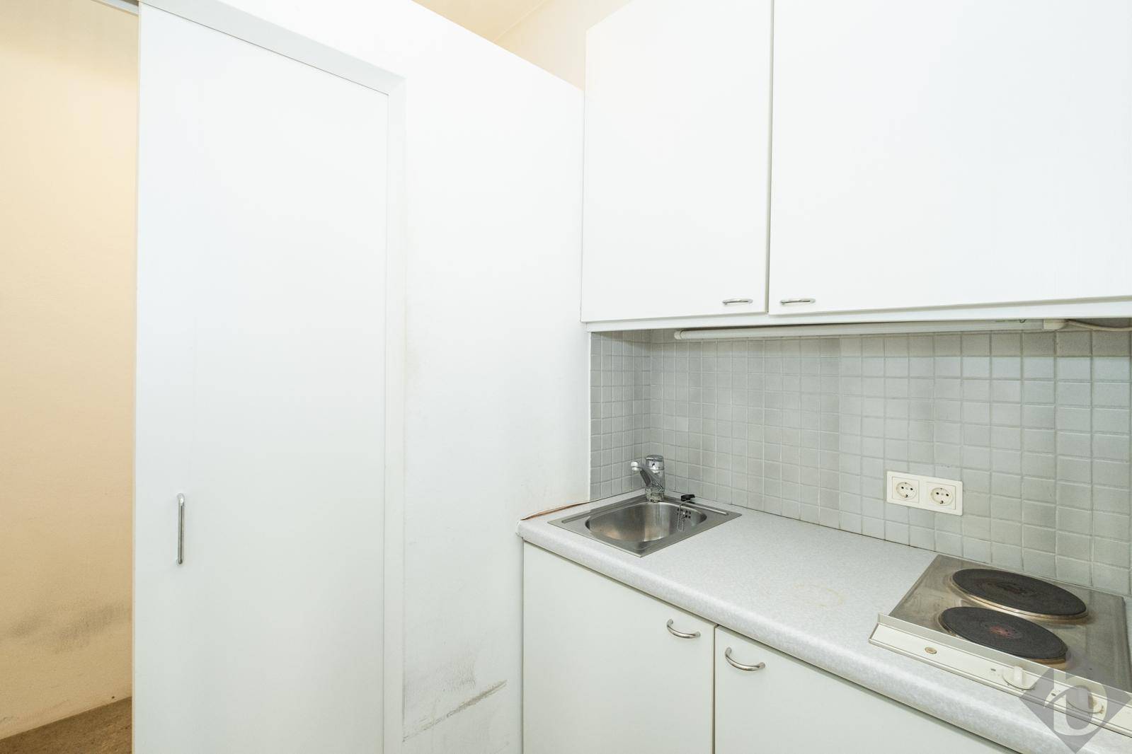 Kleine, funktionale Küchenzeile mit Spüle, Kochplatten und weißen Schränken, ideal für Pausen.