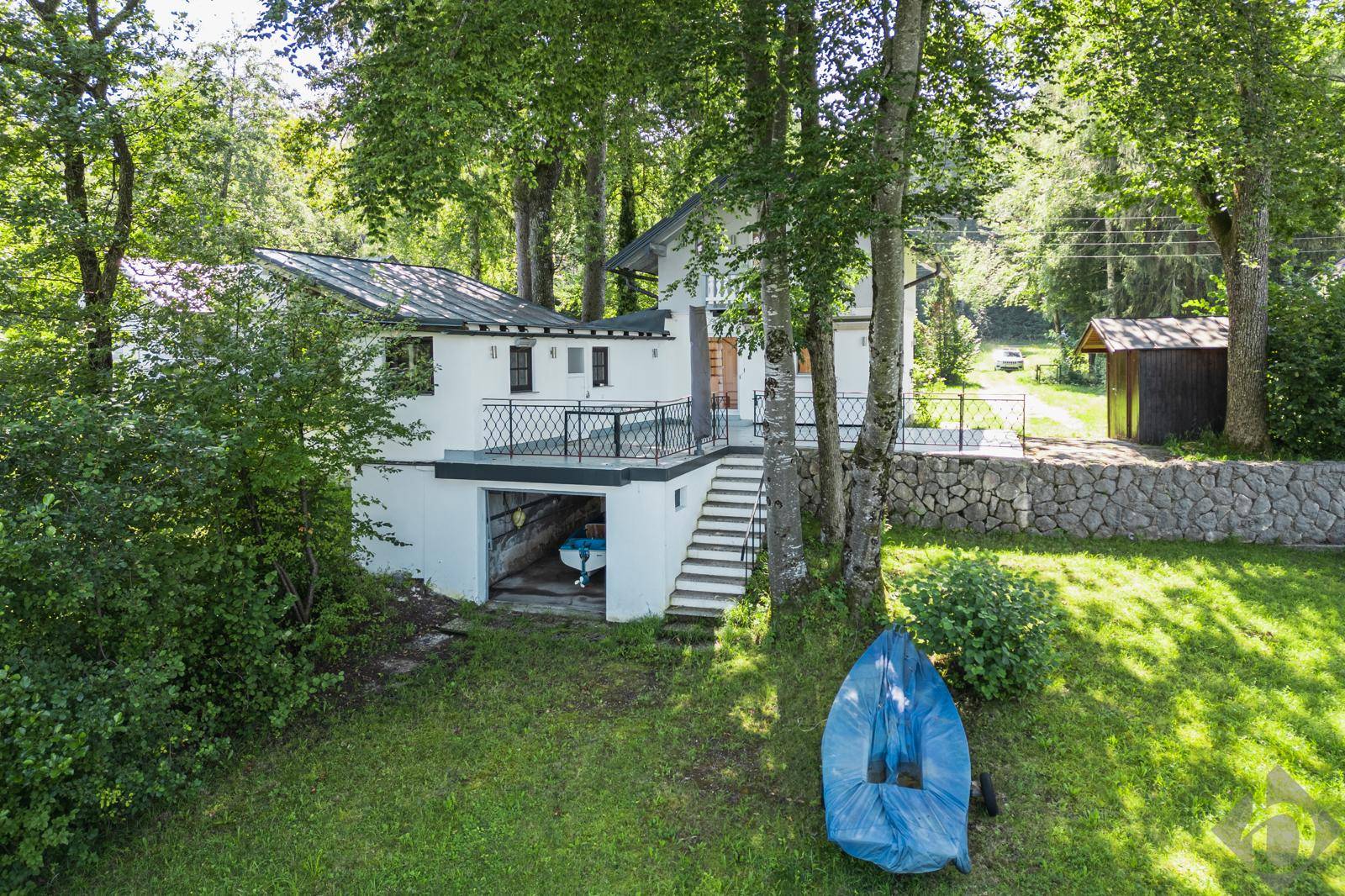 Haus mit Bootsgarage und Garten, umgeben von Bäumen, aus erhöhter Perspektive.