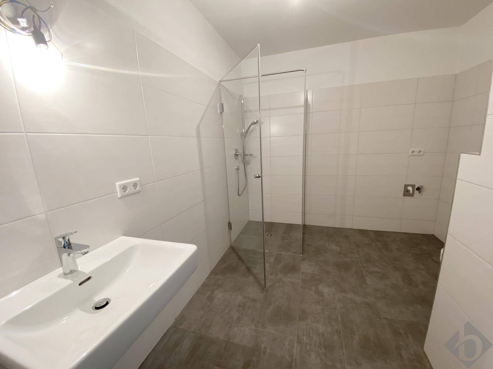 Helles Badezimmer mit ebenerdiger Dusche, Glasabtrennung und modernem Waschbecken.