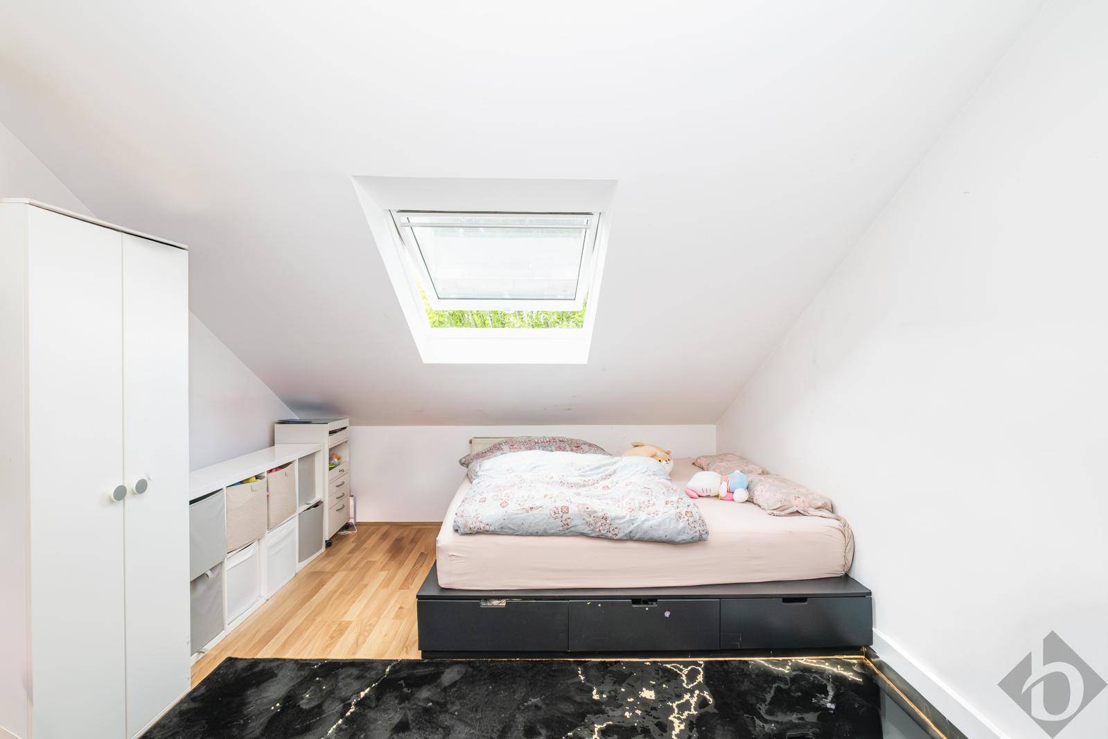 Gemütliches Schlafzimmer im Dachgeschoss mit Bett, weißem Kleiderschrank und Dachfenster.