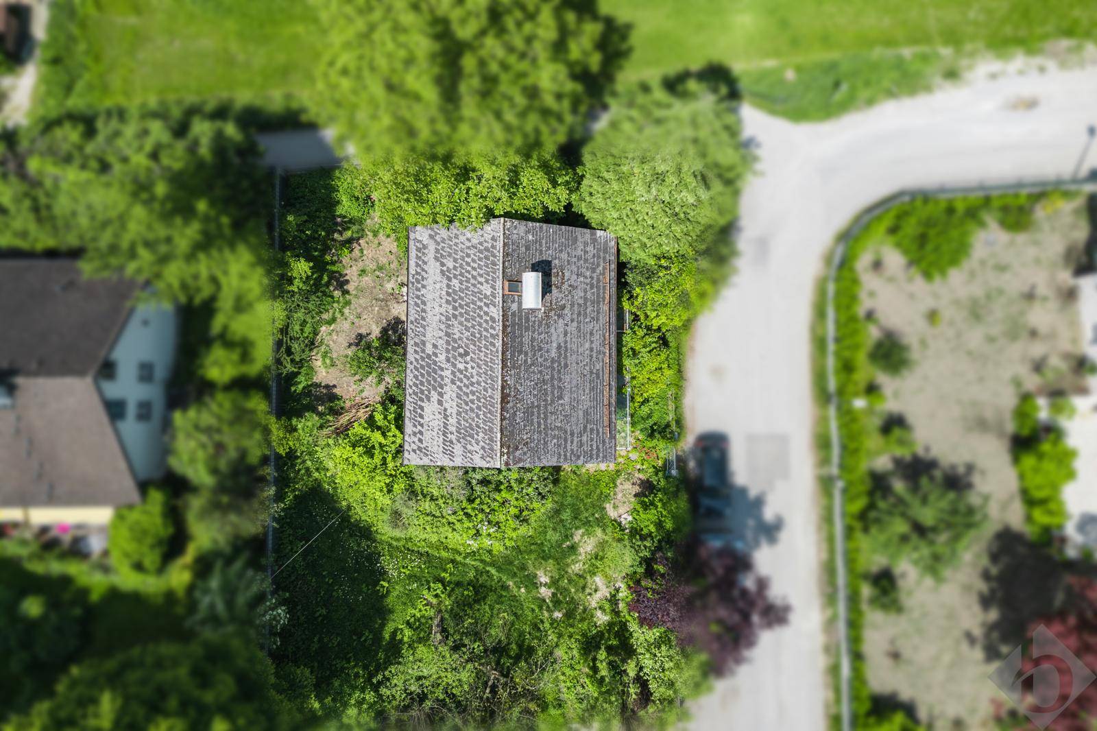 Luftaufnahme eines Hauses mit grauem Dach, umgeben von üppigem Grün und einer Zufahrtsstraße.