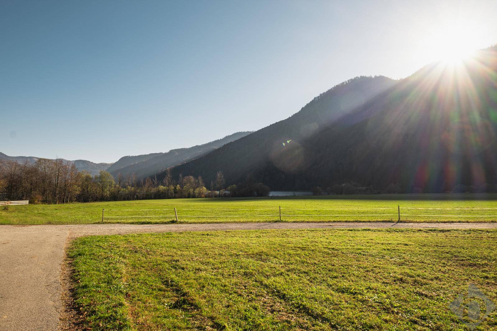 Weitläufige grüne Wiesen vor einer beeindruckenden Bergkulisse unter strahlendem Sonnenschein.