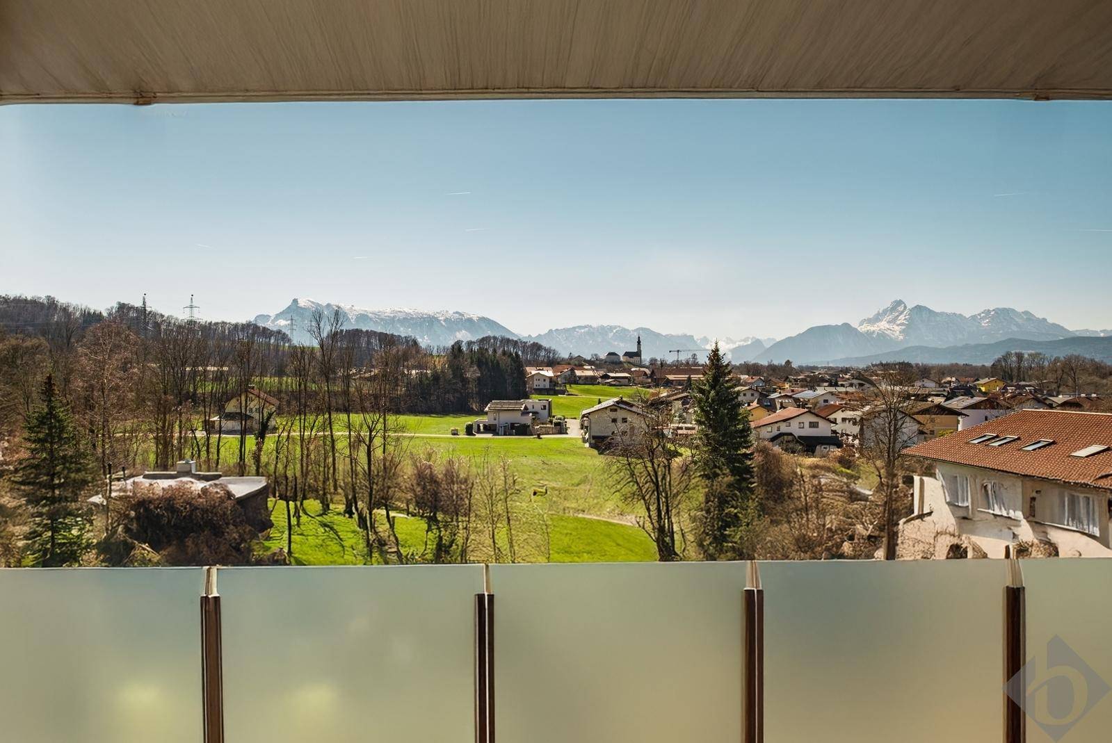 Weitläufiger Blick vom Balkon auf eine grüne Landschaft mit Häusern und schneebedeckten Bergen im Hintergrund.