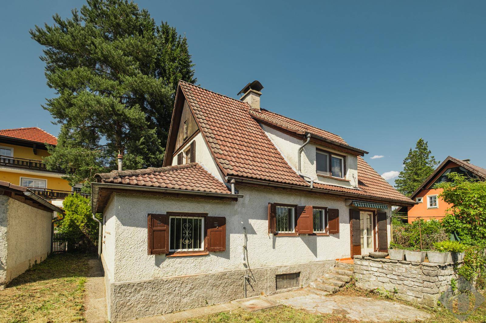 Seitenansicht des Hauses mit weißer Fassade, braunen Fensterläden und einem kleinen Terrassenbereich.