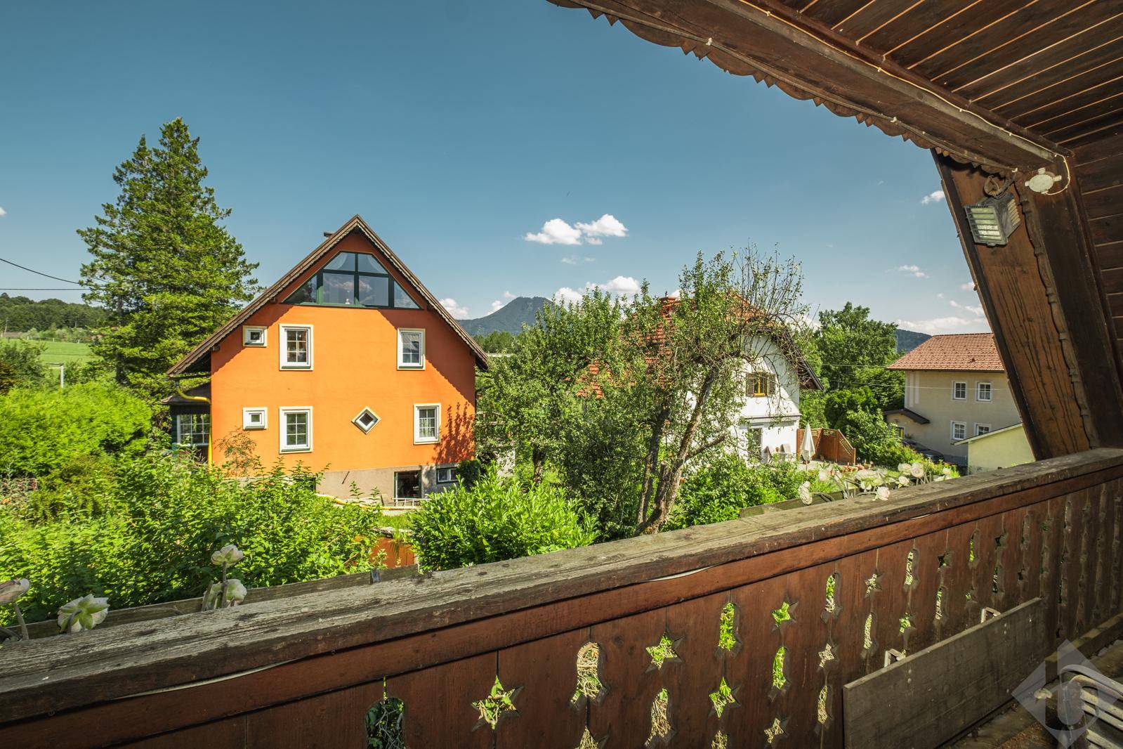 Rustikaler Holzbalkon mit Blick auf benachbarte Häuser und die umliegende grüne Landschaft.