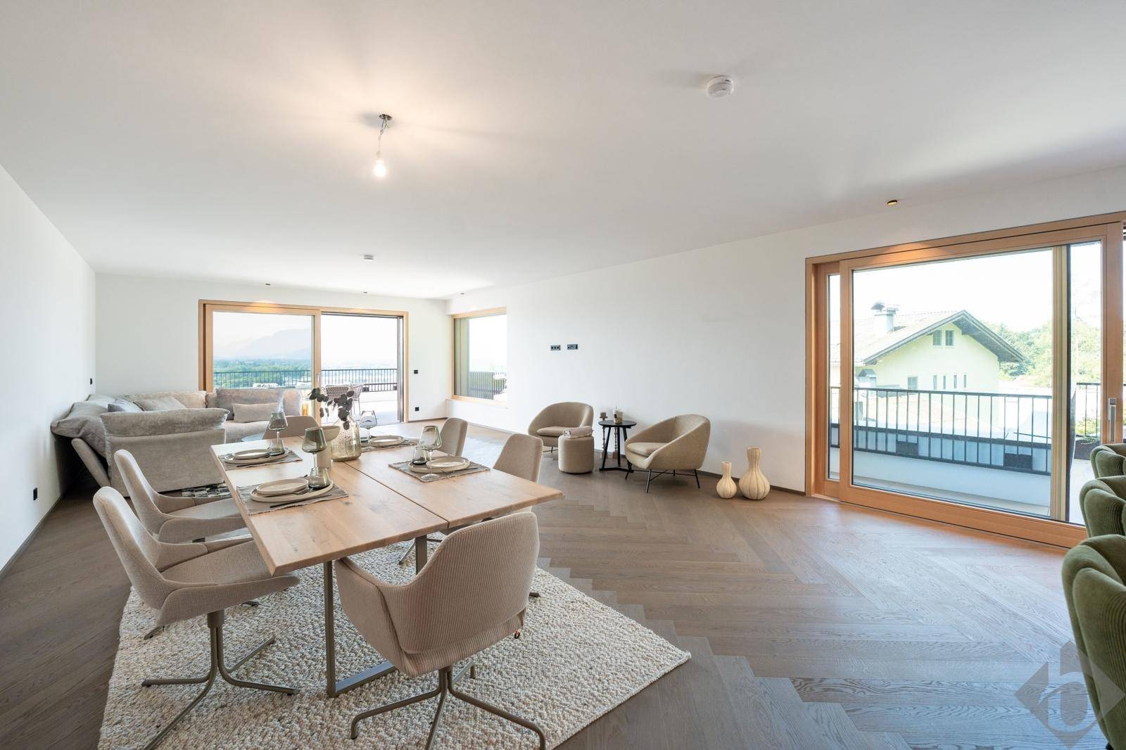 Heller Wohn- und Essbereich mit Holzboden, großen Schiebetüren und Zugang zu einem Balkon mit Aussicht.