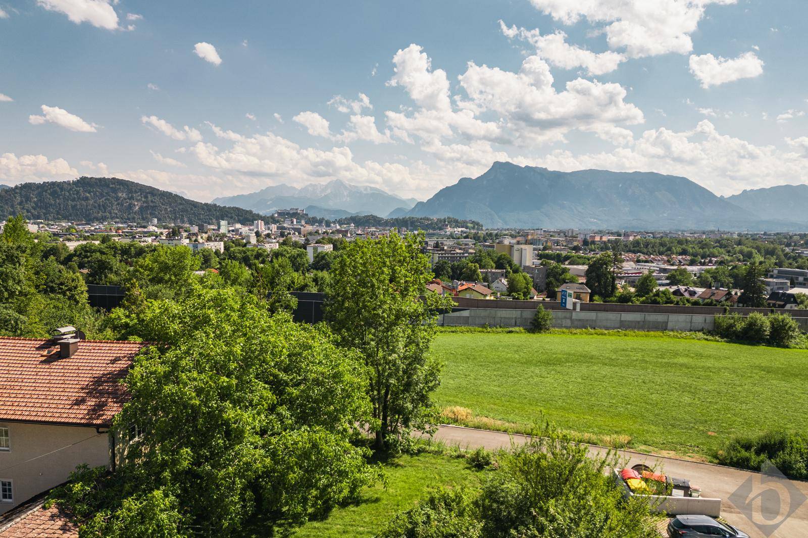 Panoramablick auf eine Stadt mit majestätischen Bergen im Hintergrund unter einem blauen Himmel.