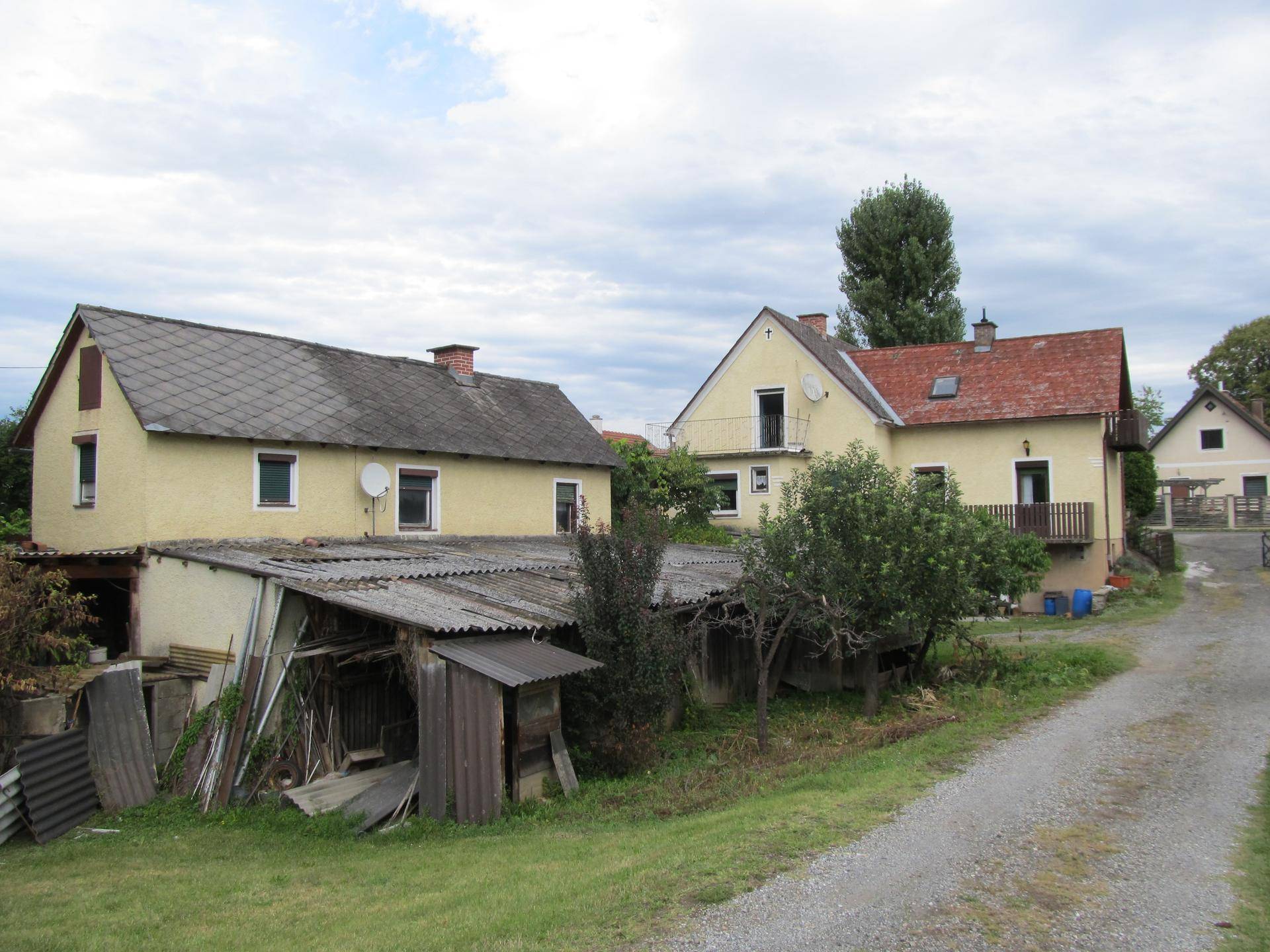Mehrere ländliche Gebäude mit unterschiedlichen Dächern und einem Schuppen auf einem weitläufigen Grundstück.