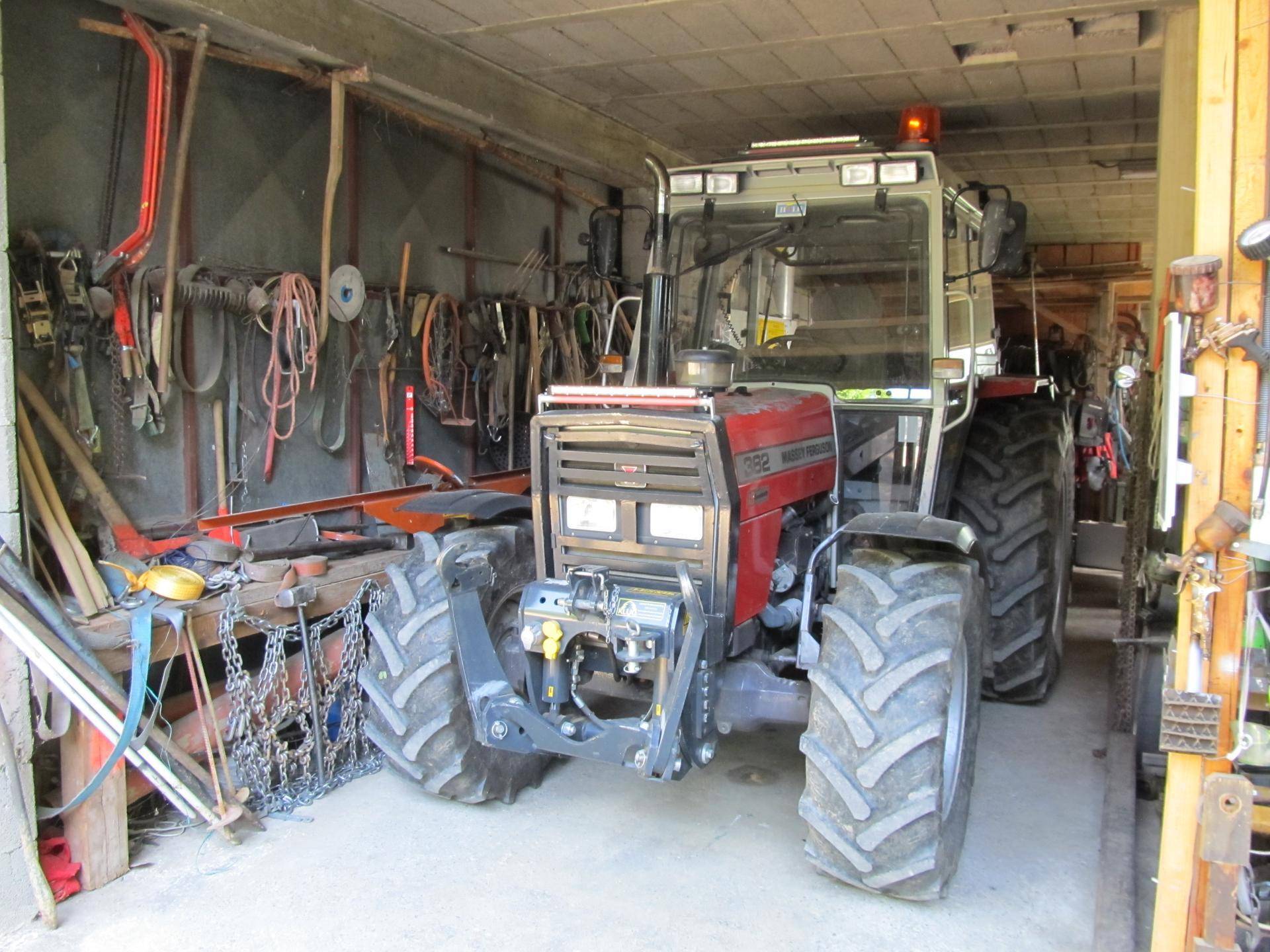 Innenansicht einer Garage oder Werkstatt mit einem großen roten Traktor und Werkzeugen an den Wänden.
