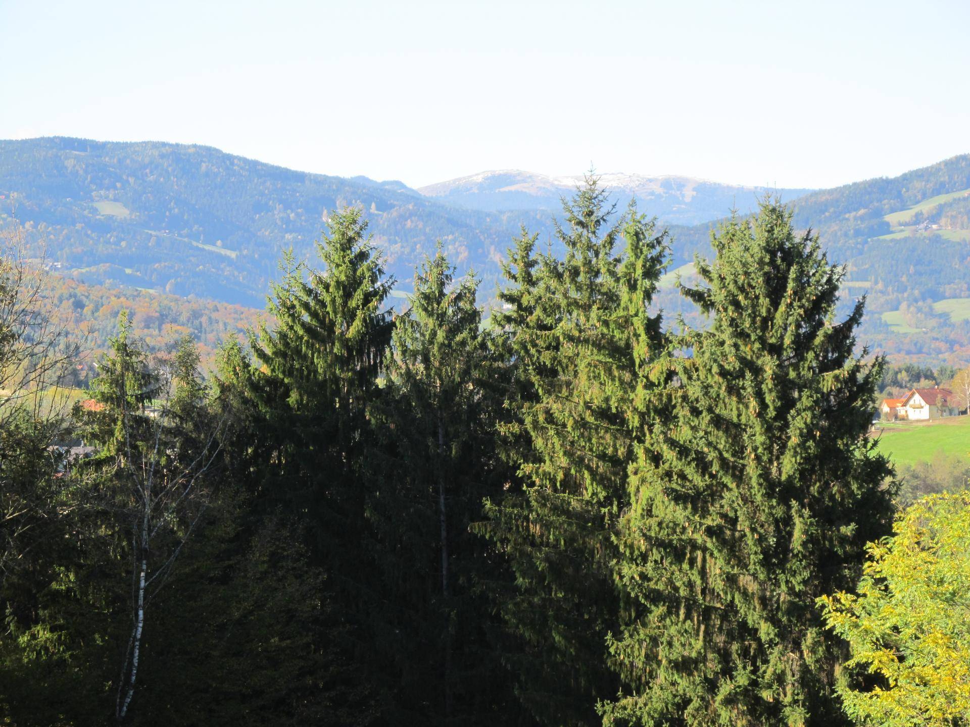 Panoramablick auf bewaldete Berge und Täler mit vereinzelten Häusern in der Ferne.