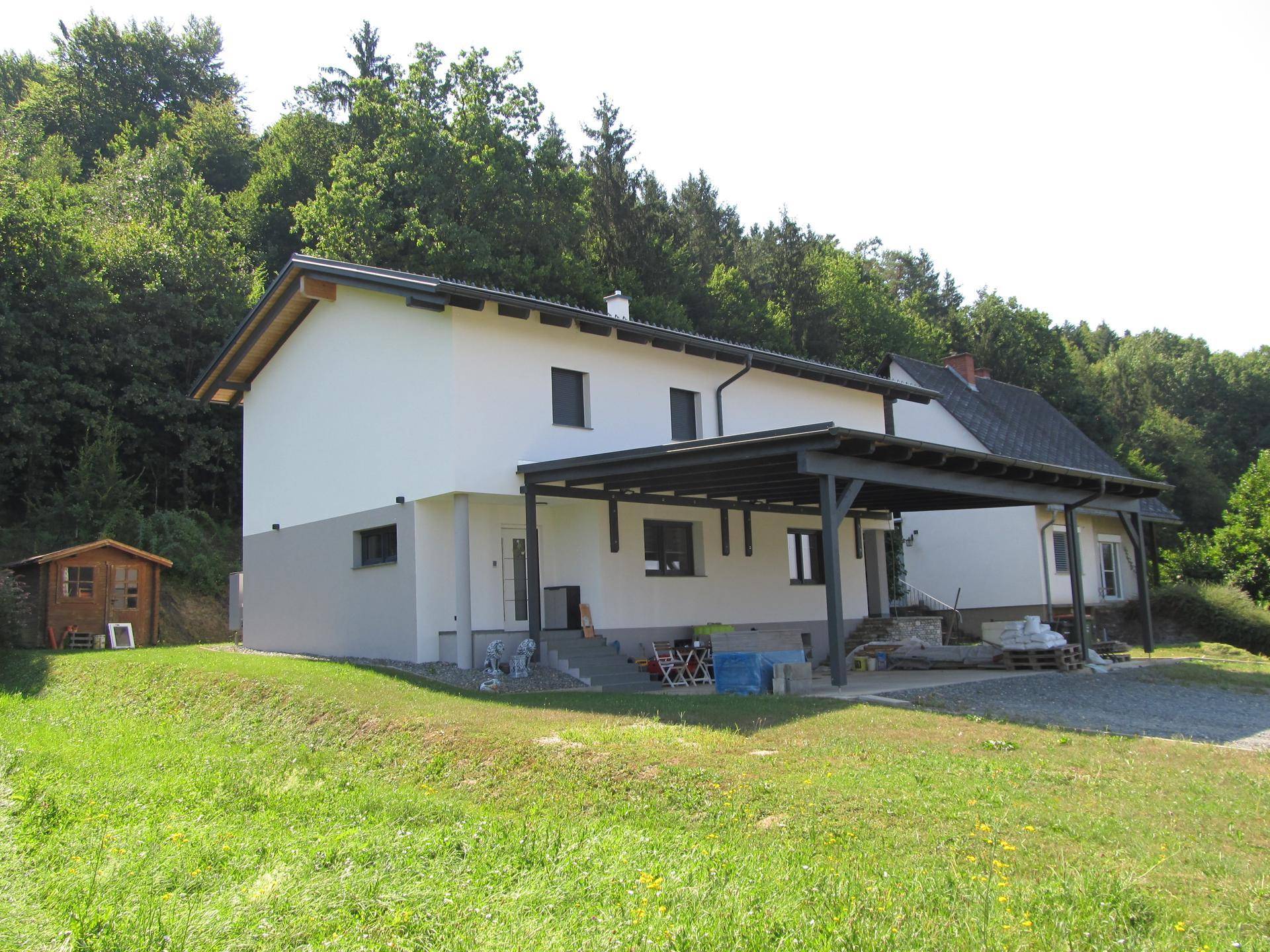 Rückansicht des modernen Hauses mit Carport und Blick auf den bewaldeten Hügel.