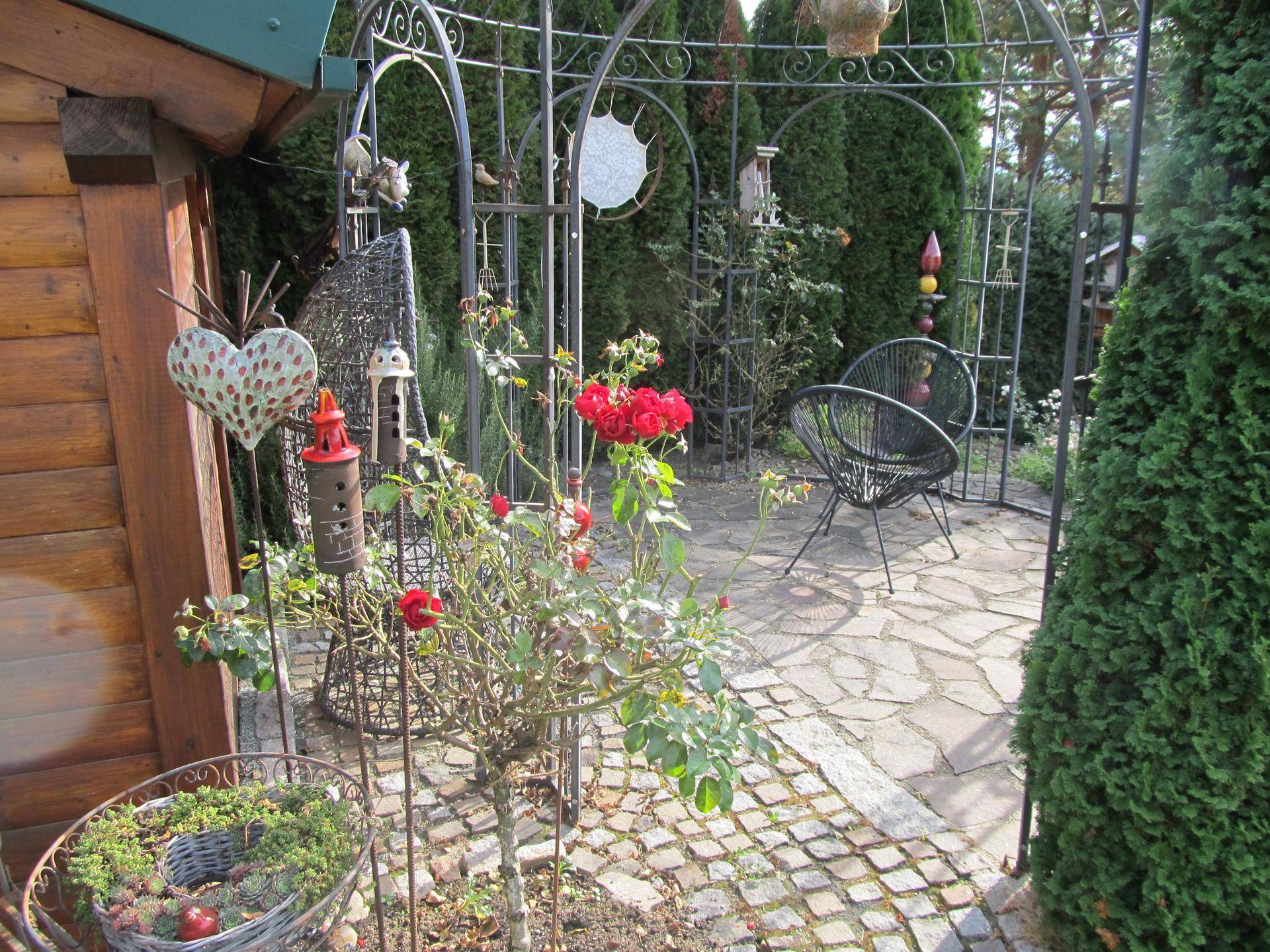 Blühender Gartenbereich mit Rosen, einem dekorativen Metallpavillon und gepflastertem Boden.