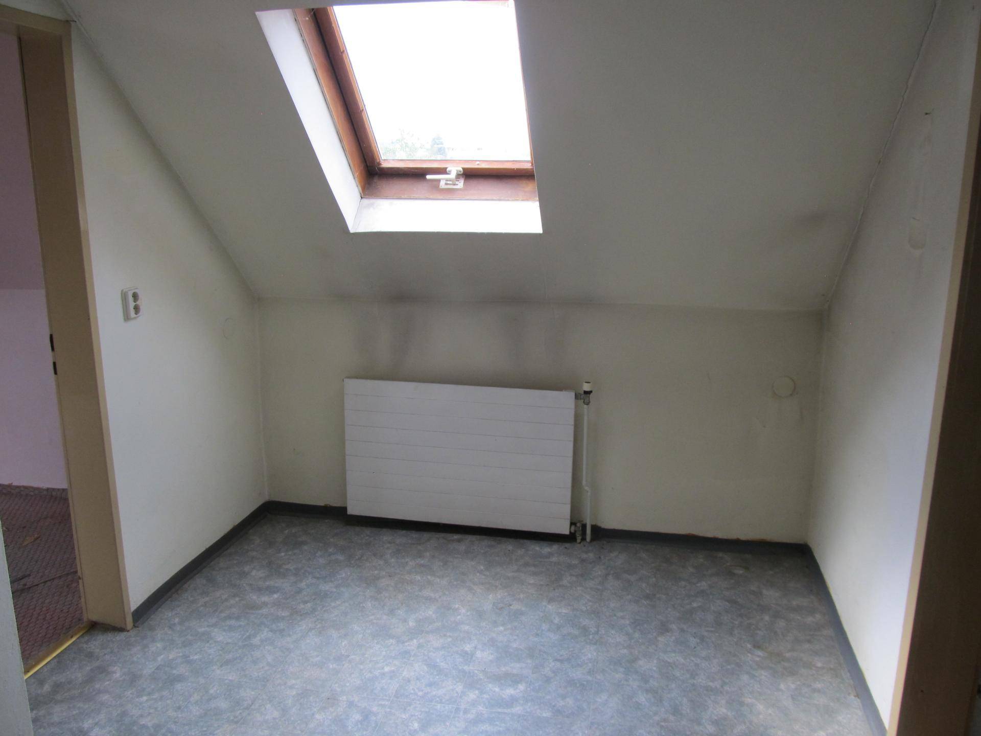 Helles Dachzimmer mit schrägen Wänden, Dachfenster, grauem Boden und einem Heizkörper.