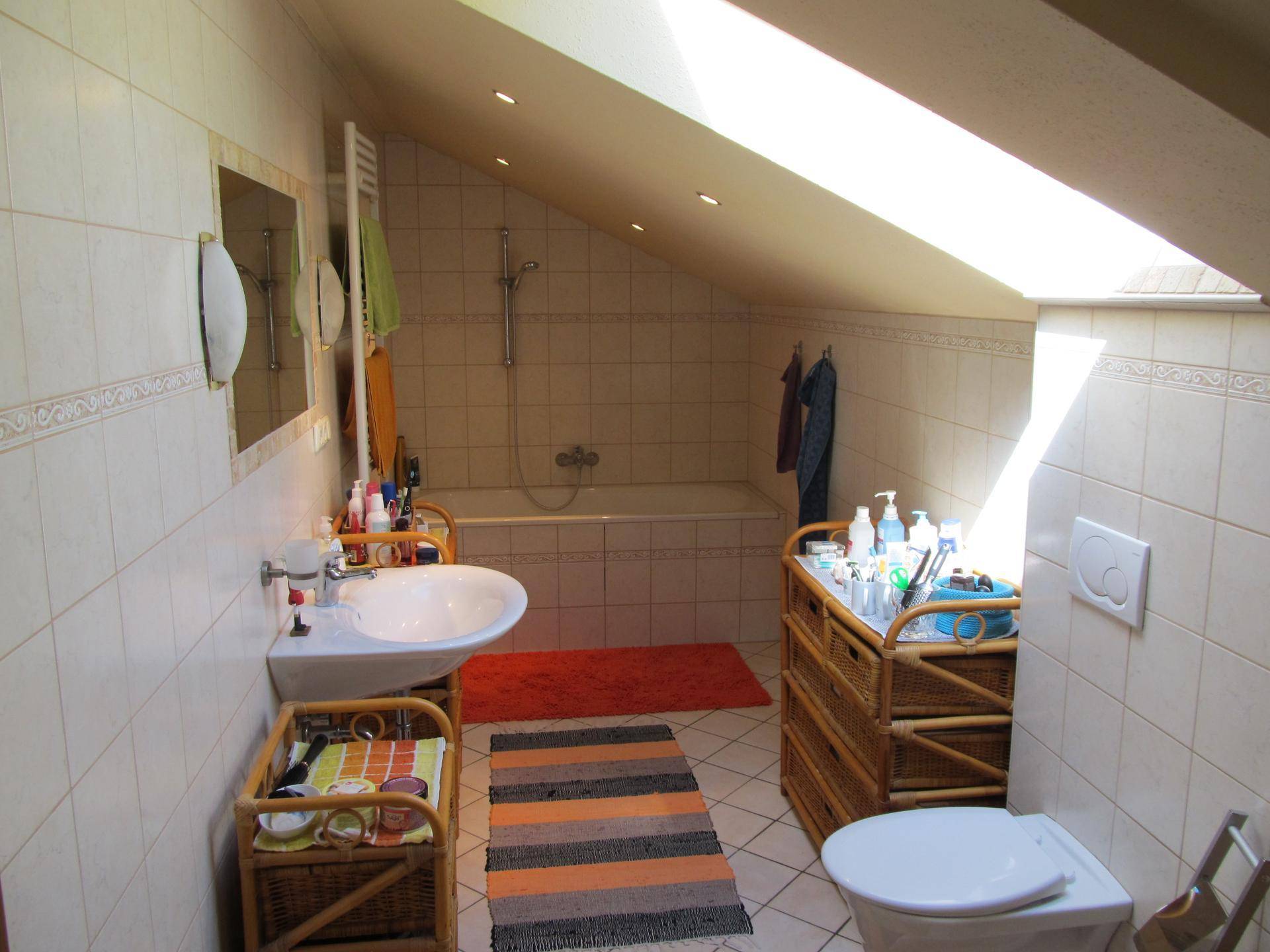 Helles Dachgeschoss-Badezimmer mit Badewanne, Waschbecken und Dachfenster für viel Licht.