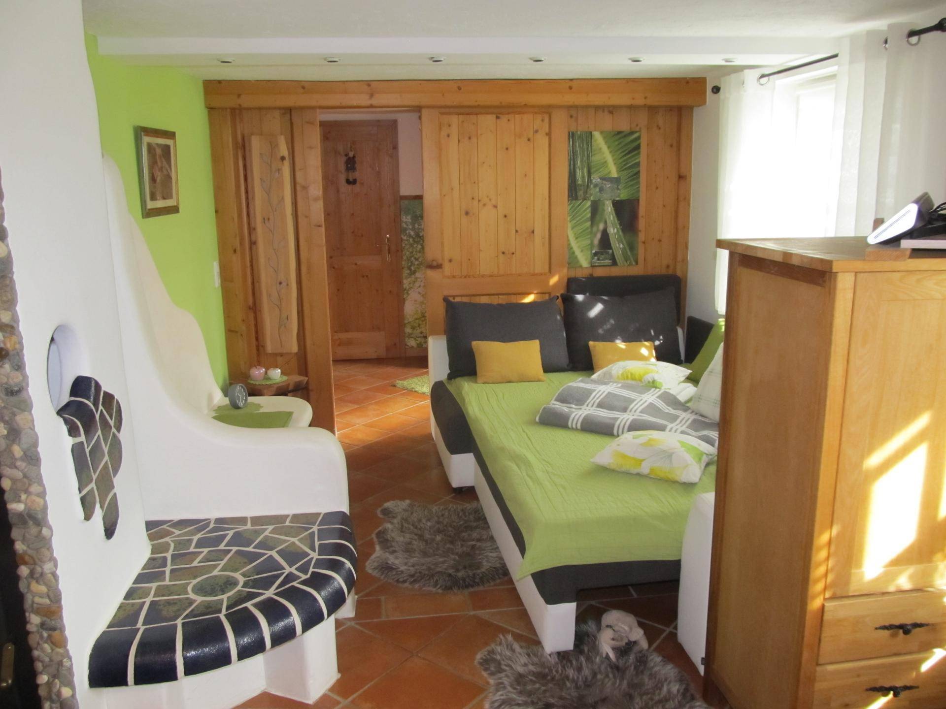 Gemütlicher Wohn- und Schlafbereich mit Bett, Holzwänden und Terrakottafliesen.