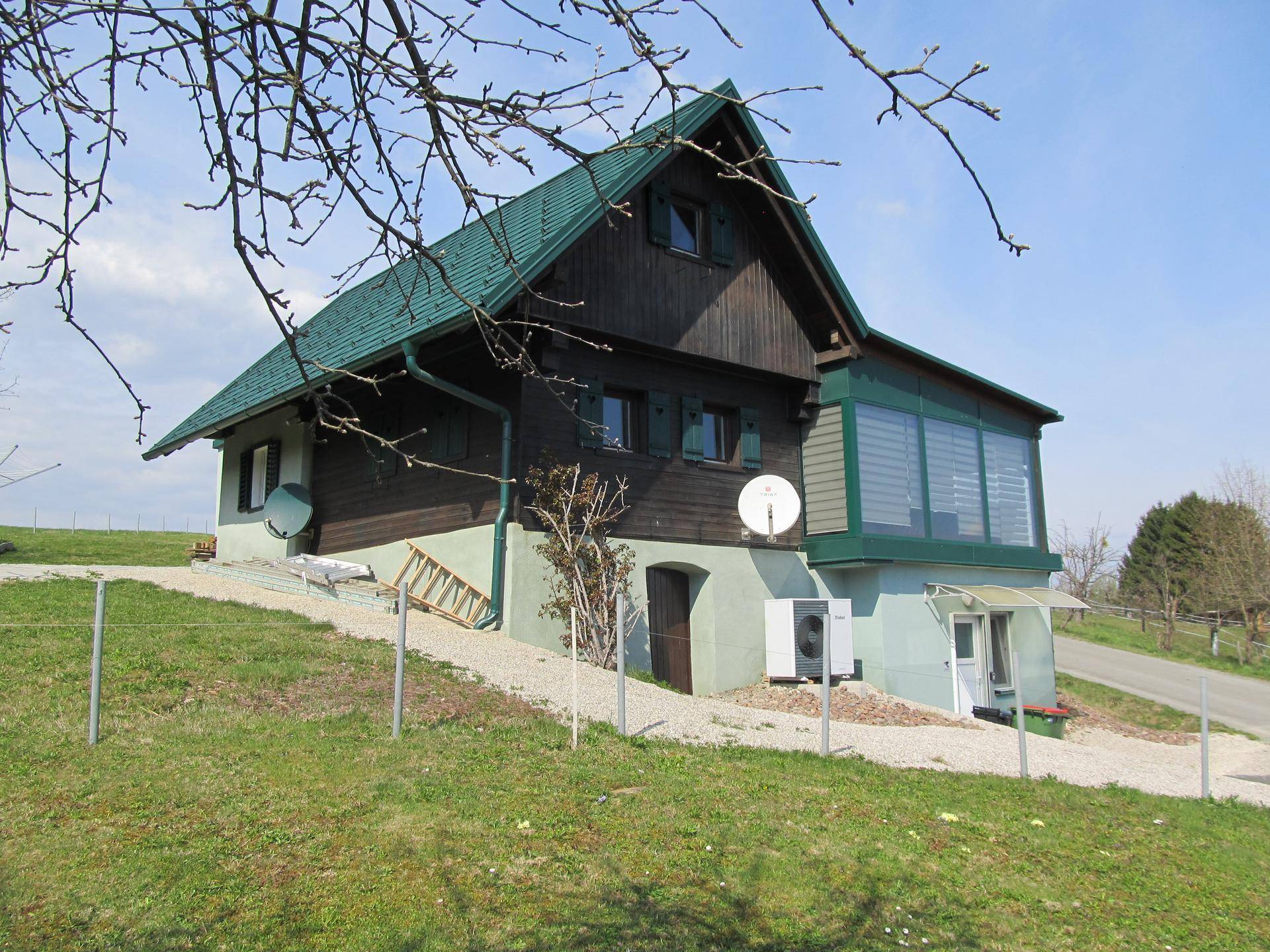 Hausfassade mit Holzverkleidung und grünem Dach vor blauem Himmel in ländlicher Umgebung.