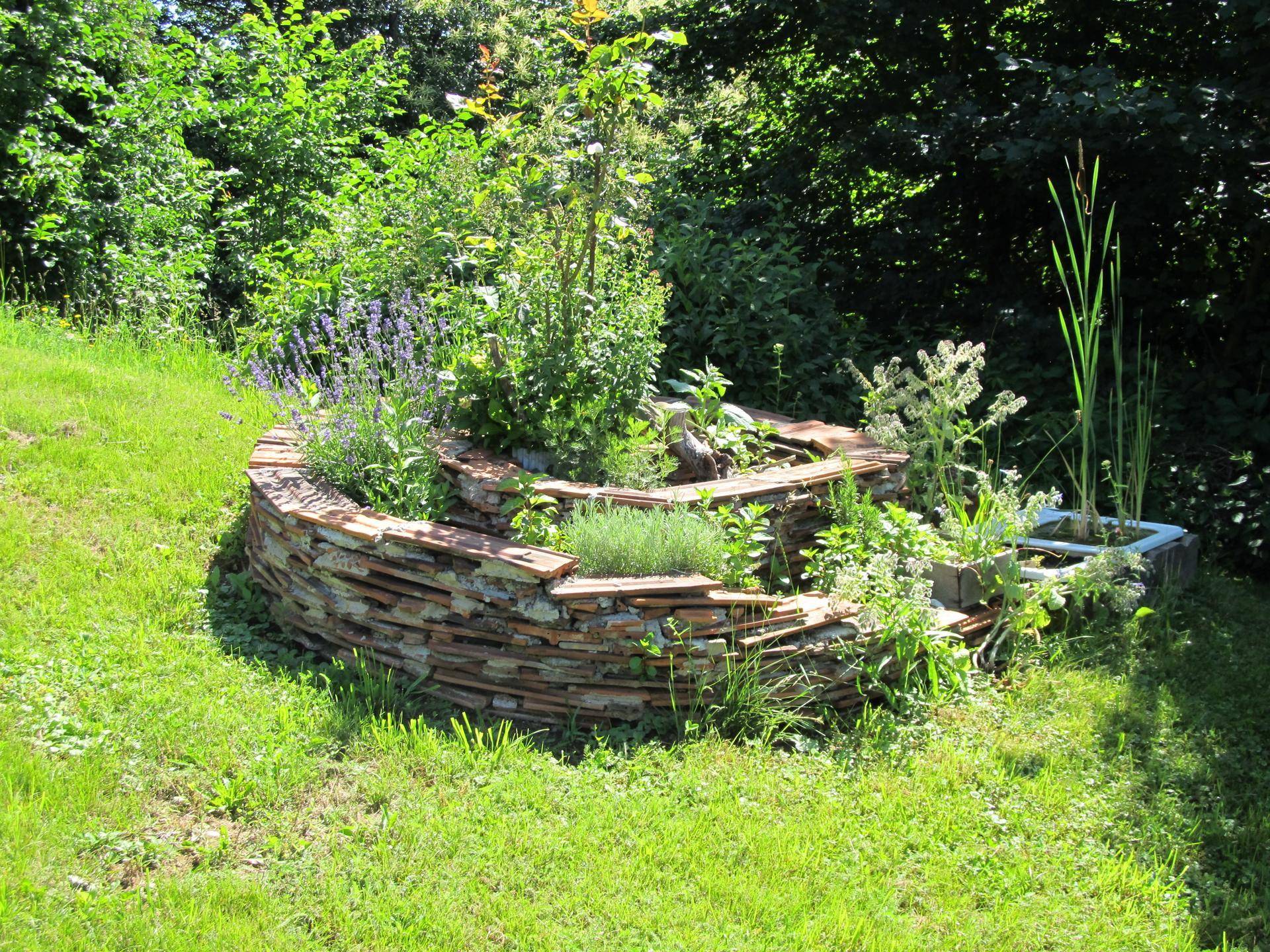 Kreativ gestaltetes Hochbeet aus Naturstein mit verschiedenen Kräutern und Pflanzen im Garten.