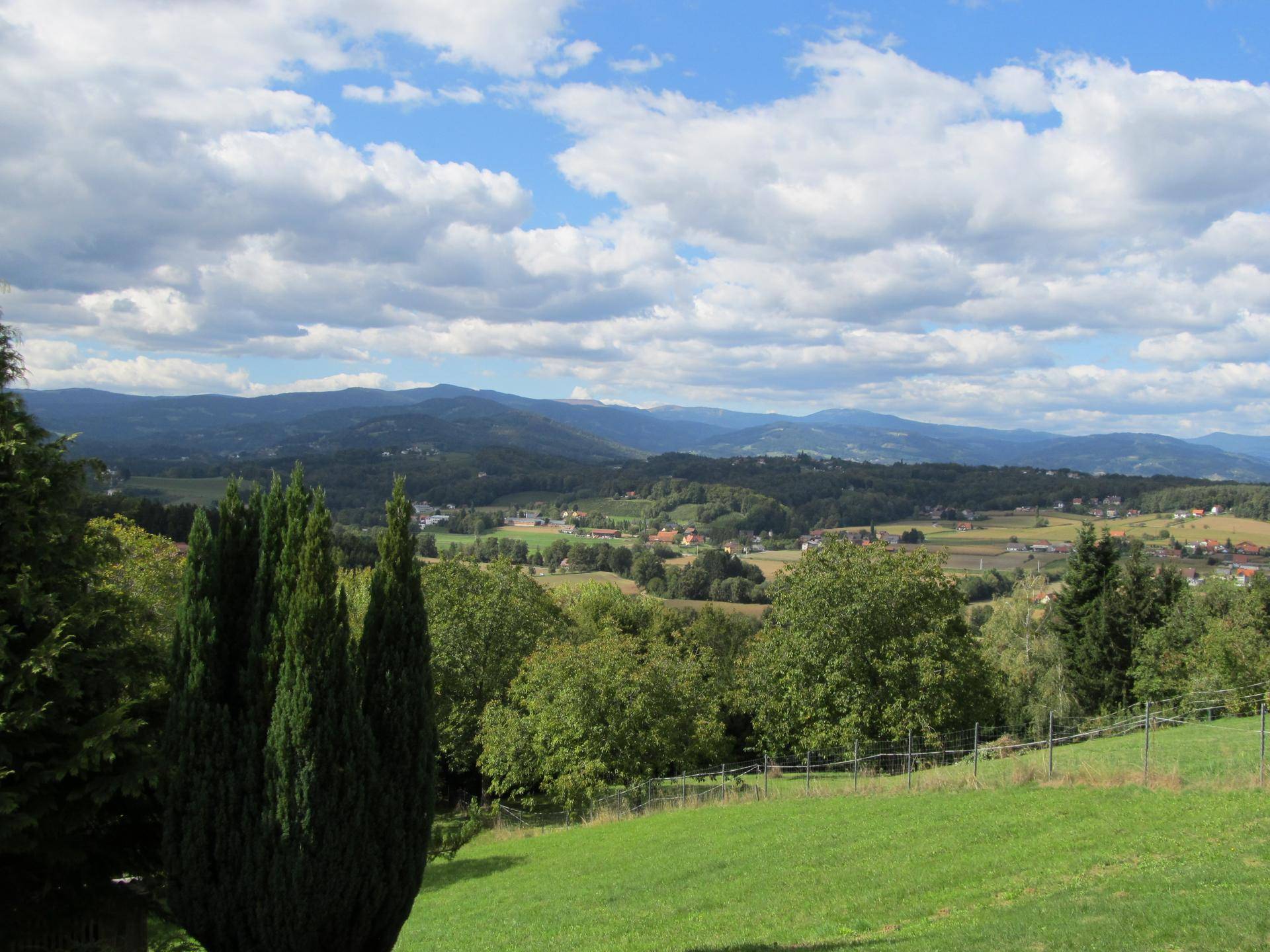 Atemberaubender Weitblick über die hügelige Landschaft mit Wäldern und entfernten Siedlungen unter blauem Himmel.