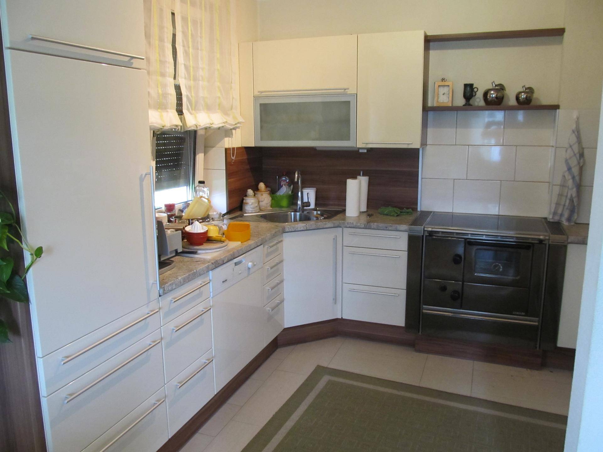 Helle Einbauküche mit weißen Fronten, Holzdetails und traditionellem Ofen.