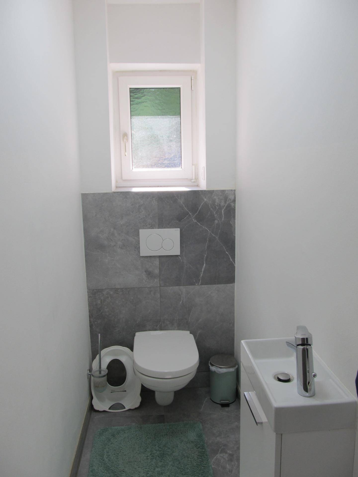 Kleines Gäste-WC mit wandhängender Toilette, Waschbecken und Fenster.