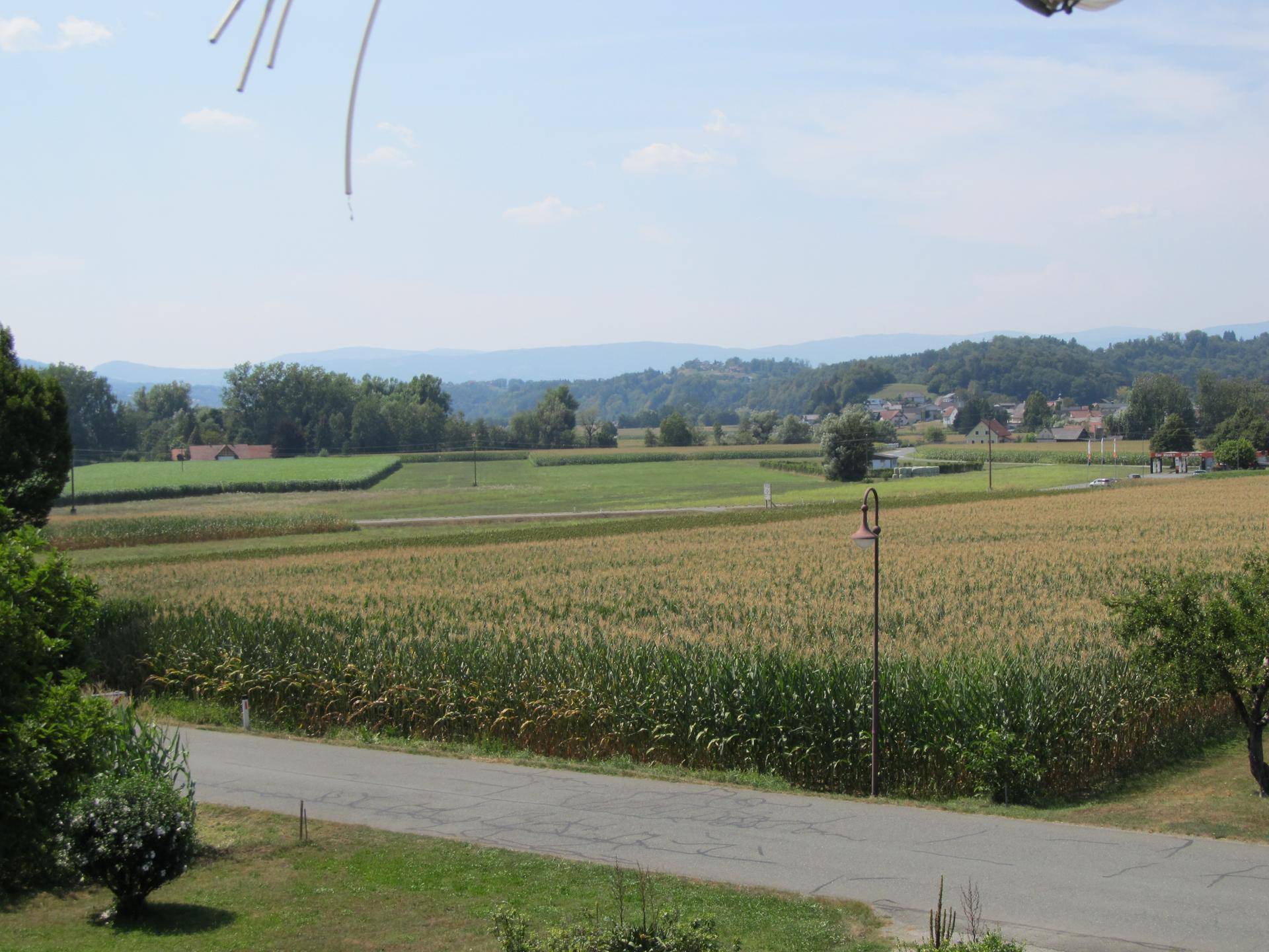 Weitläufiger Blick über grüne Felder und ländliche Umgebung mit Hügeln im Hintergrund.