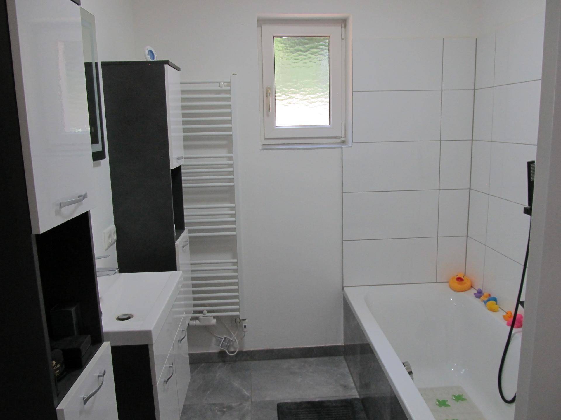 Modernes Badezimmer mit Badewanne, weißen Fliesen und beheiztem Handtuchhalter.