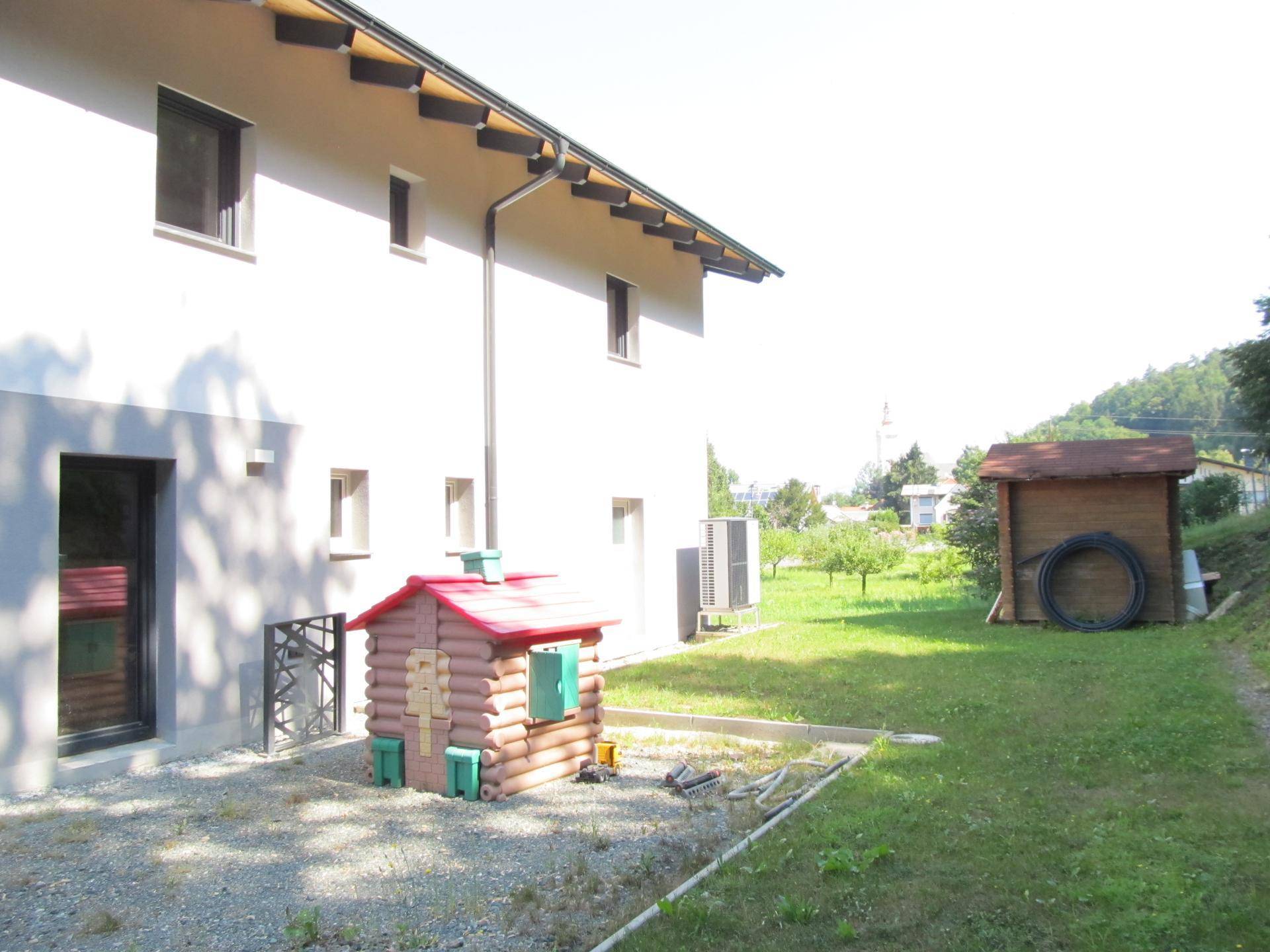 Seitenansicht des Hauses mit Kinderspielhaus und einem Holzschuppen im grünen Gartenbereich.