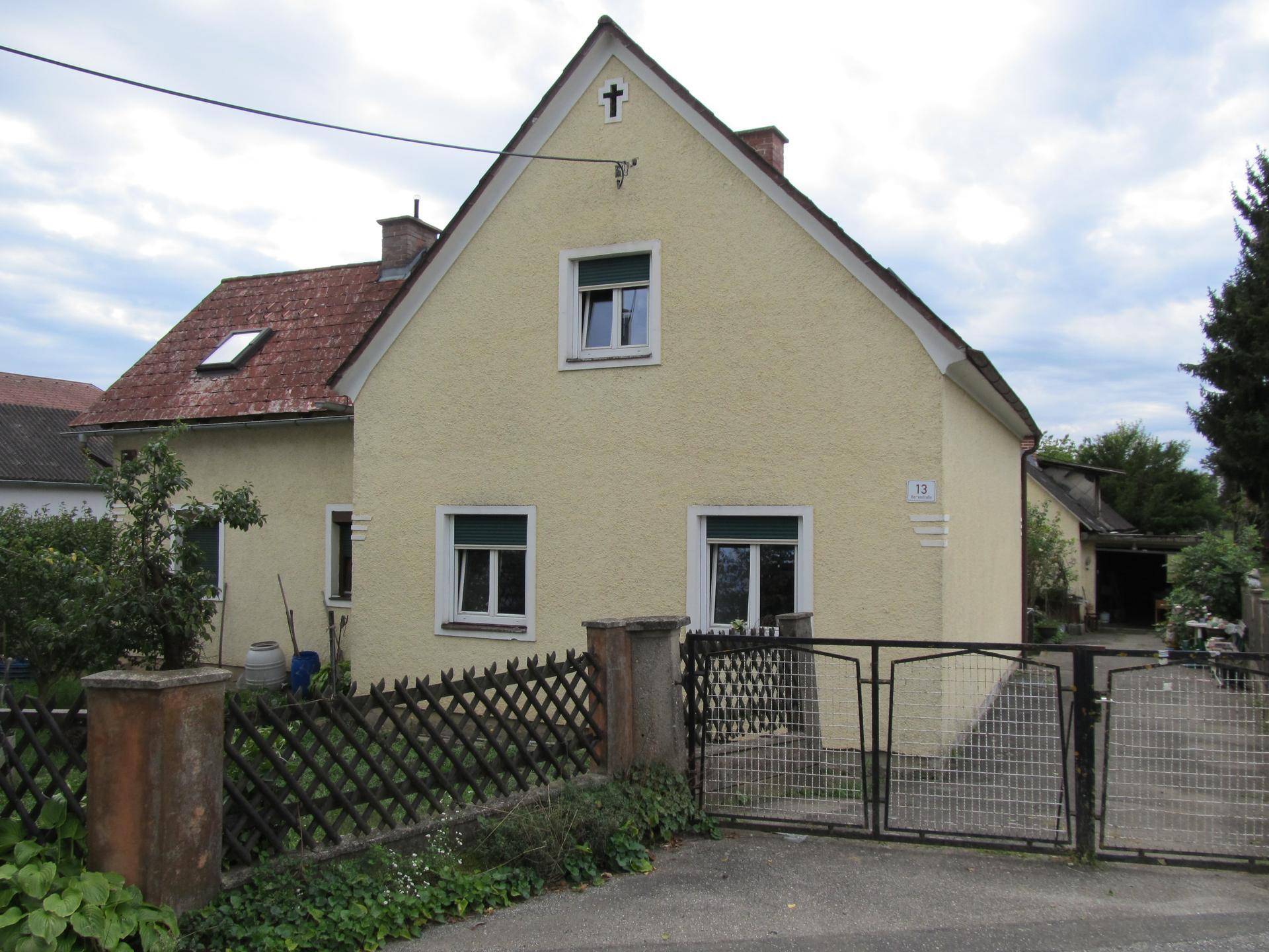 Vorderansicht eines gelben Einfamilienhauses mit Satteldach, weißen Fenstern und einem Gartentor.