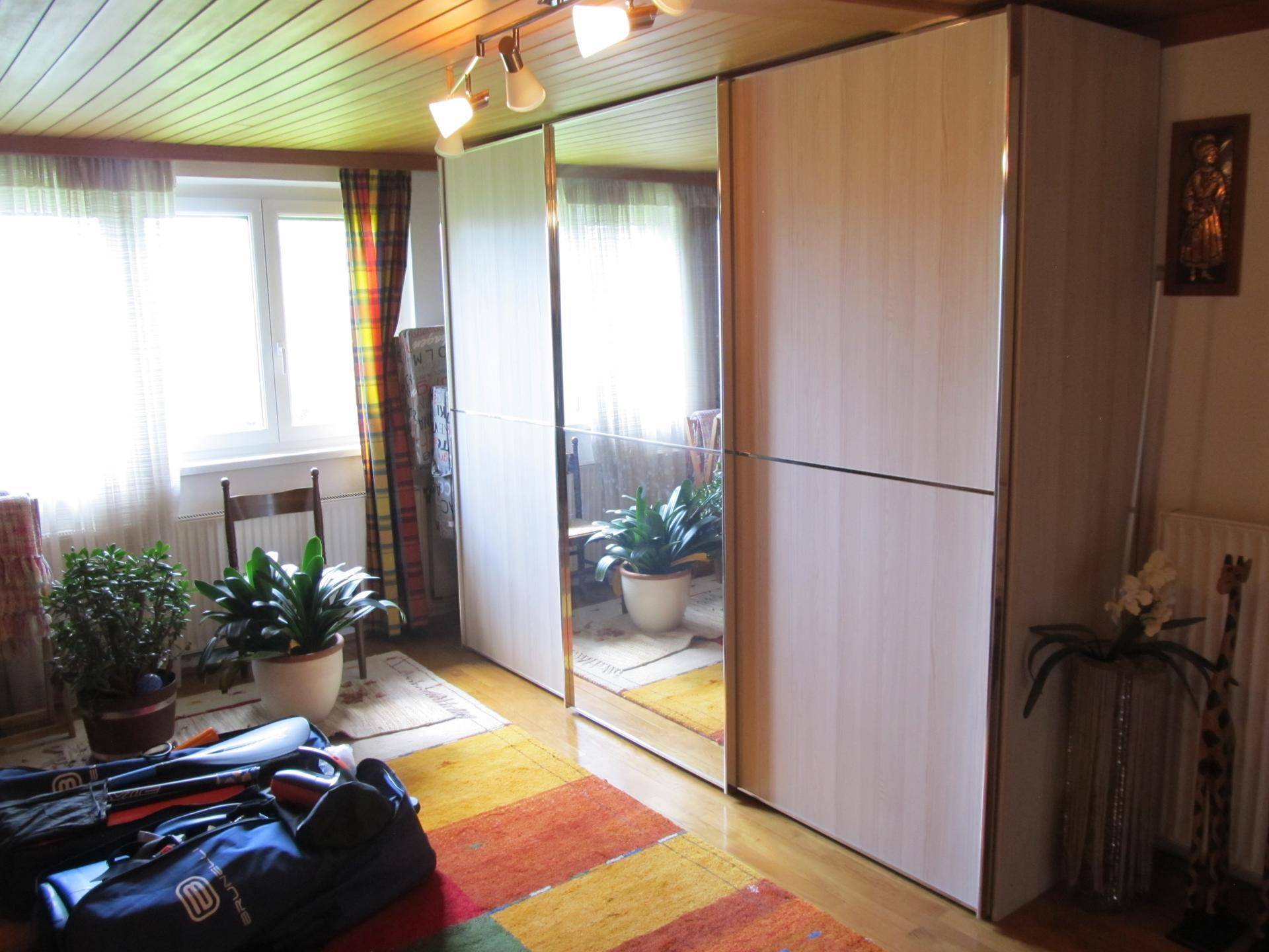 Schlafzimmer mit Spiegelschränken, Holzboden und einem Fenster, das viel Tageslicht hereinlässt.