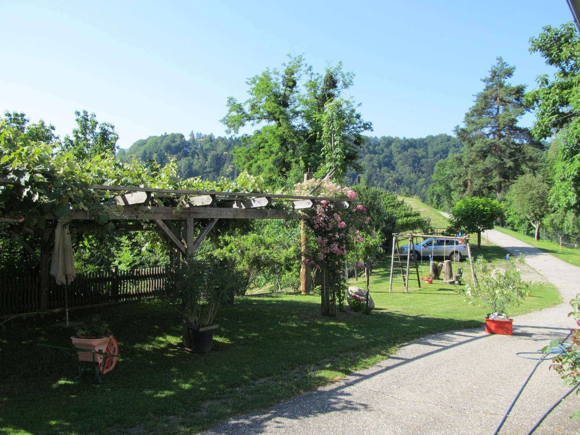 Idyllischer Gartenbereich mit bewachsener Holzpergola, Schaukel und Blick auf die Landschaft.
