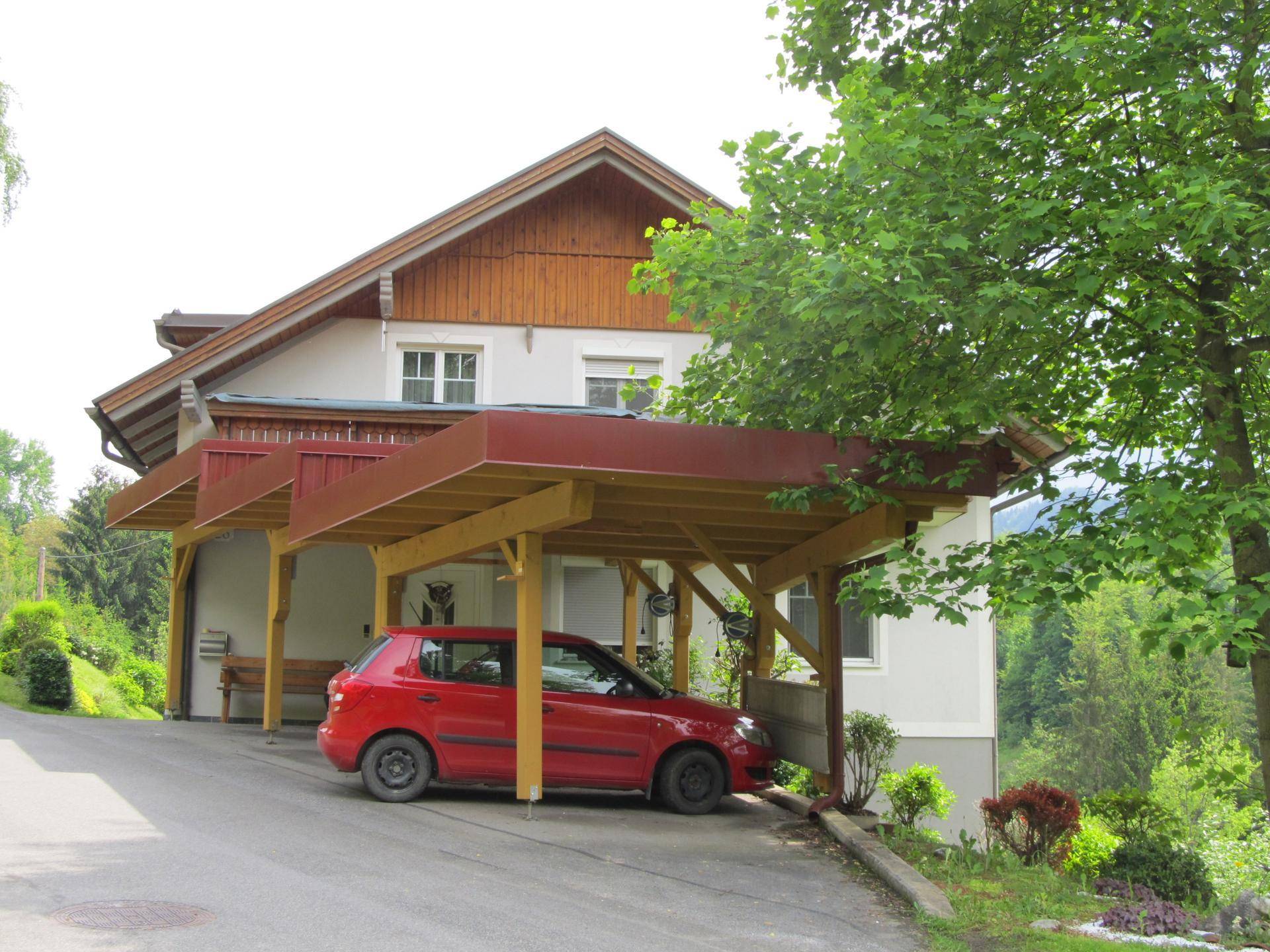 Hausfassade mit Holzverkleidung und einem überdachten Carport für ein Fahrzeug.