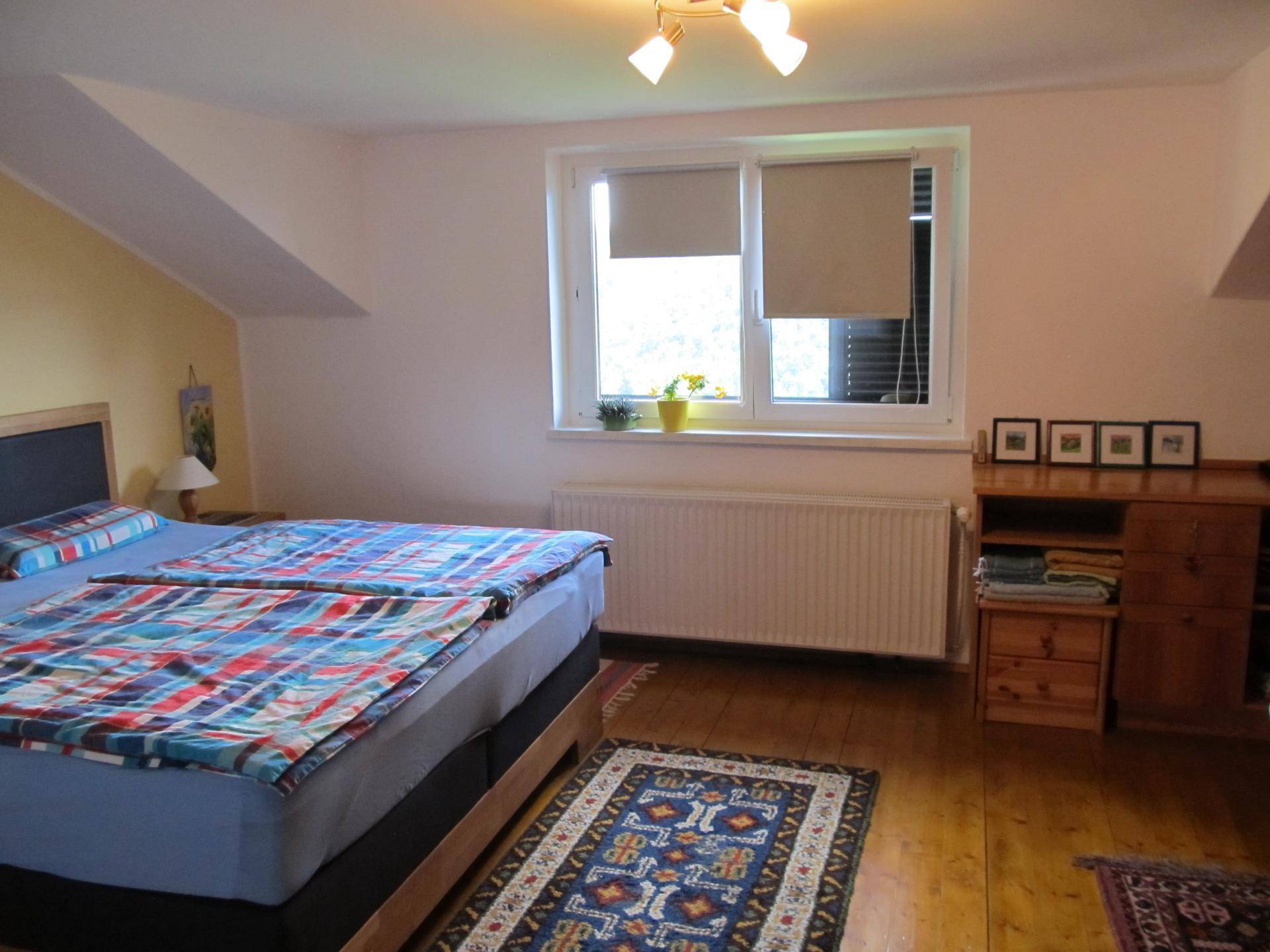 Gemütliches Schlafzimmer im Dachgeschoss mit Doppelbett, Holzboden und Fensterblick ins Grüne.