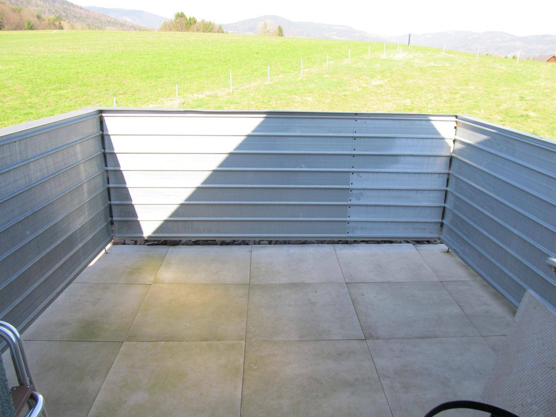 Gepflasterte Terrasse mit hohen Wänden und Blick auf die grüne Landschaft.