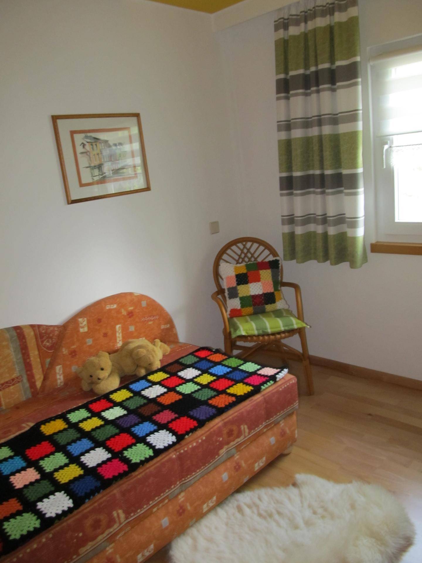 Gemütliches Schlafzimmer mit Einzelbett, Holzboden und farbenfroher Dekoration.