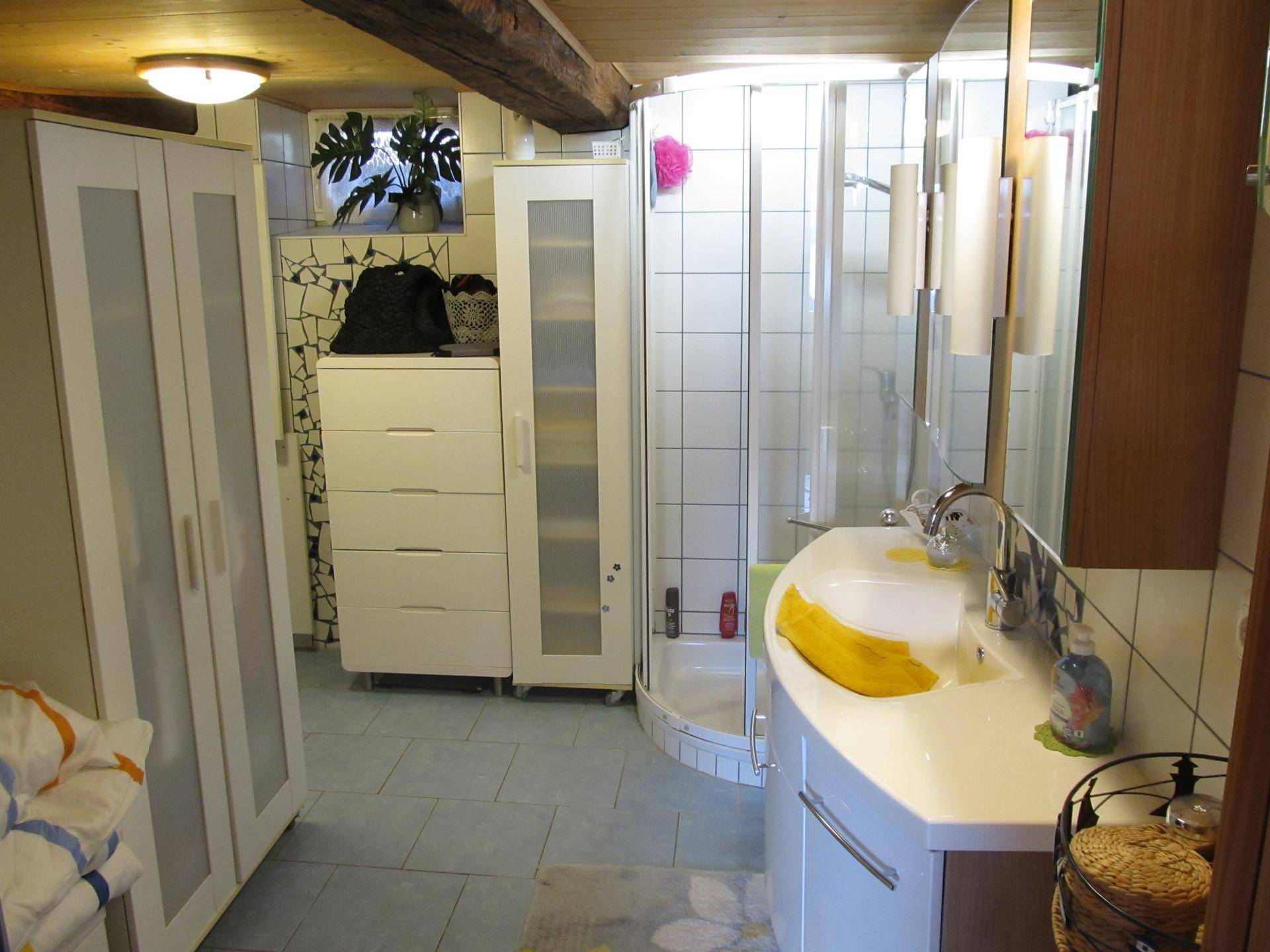 Badezimmer mit Duschkabine, Waschtisch und weißen Fliesen.